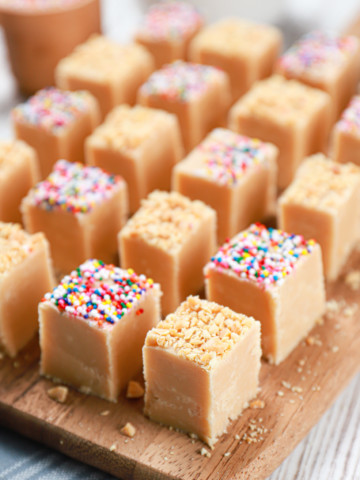 Side view of a batch of peanut butter fudge cut into pieces on a wooden cutting board.