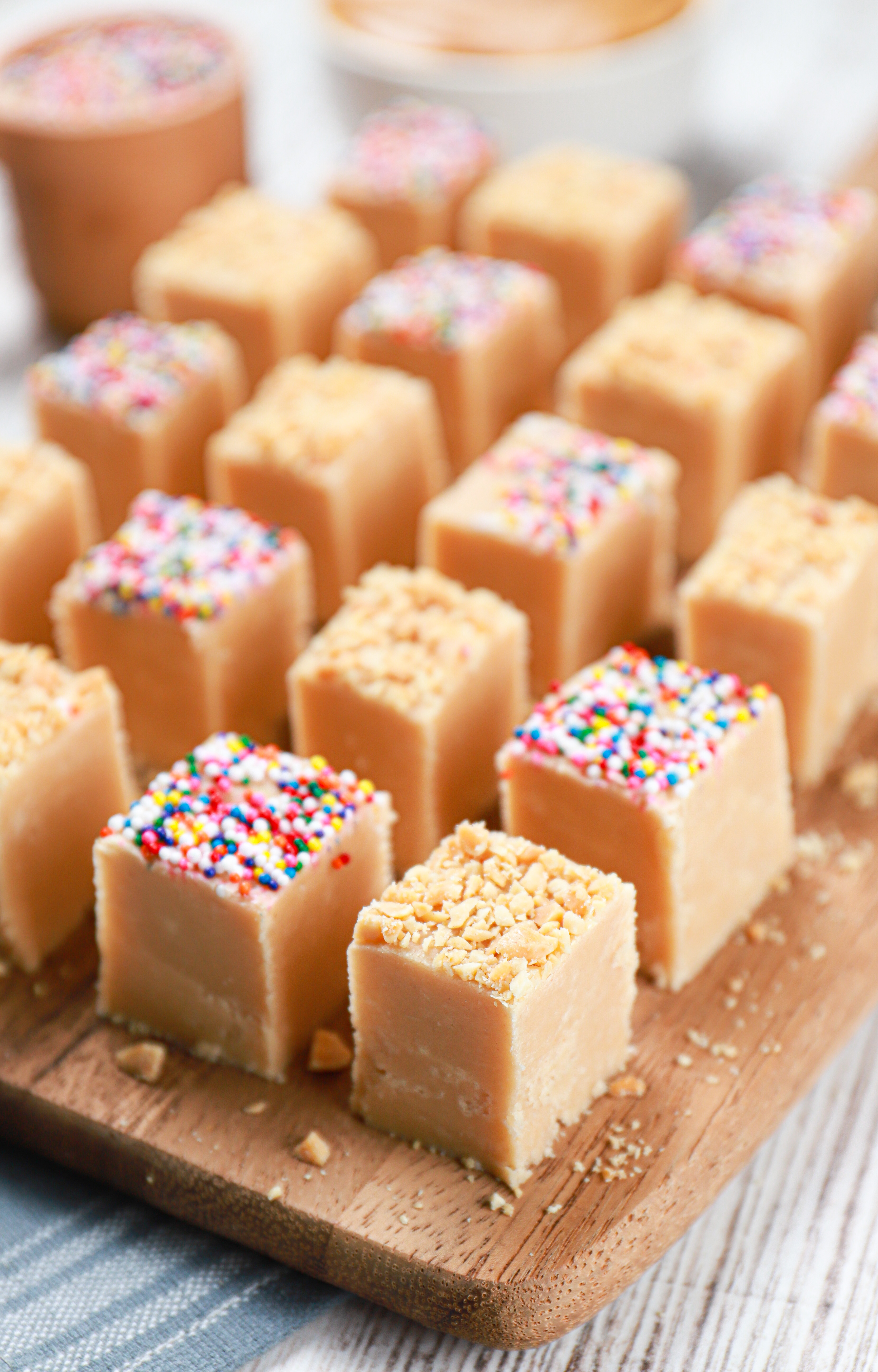 Side view of a batch of peanut butter fudge cut into pieces on a wooden cutting board.