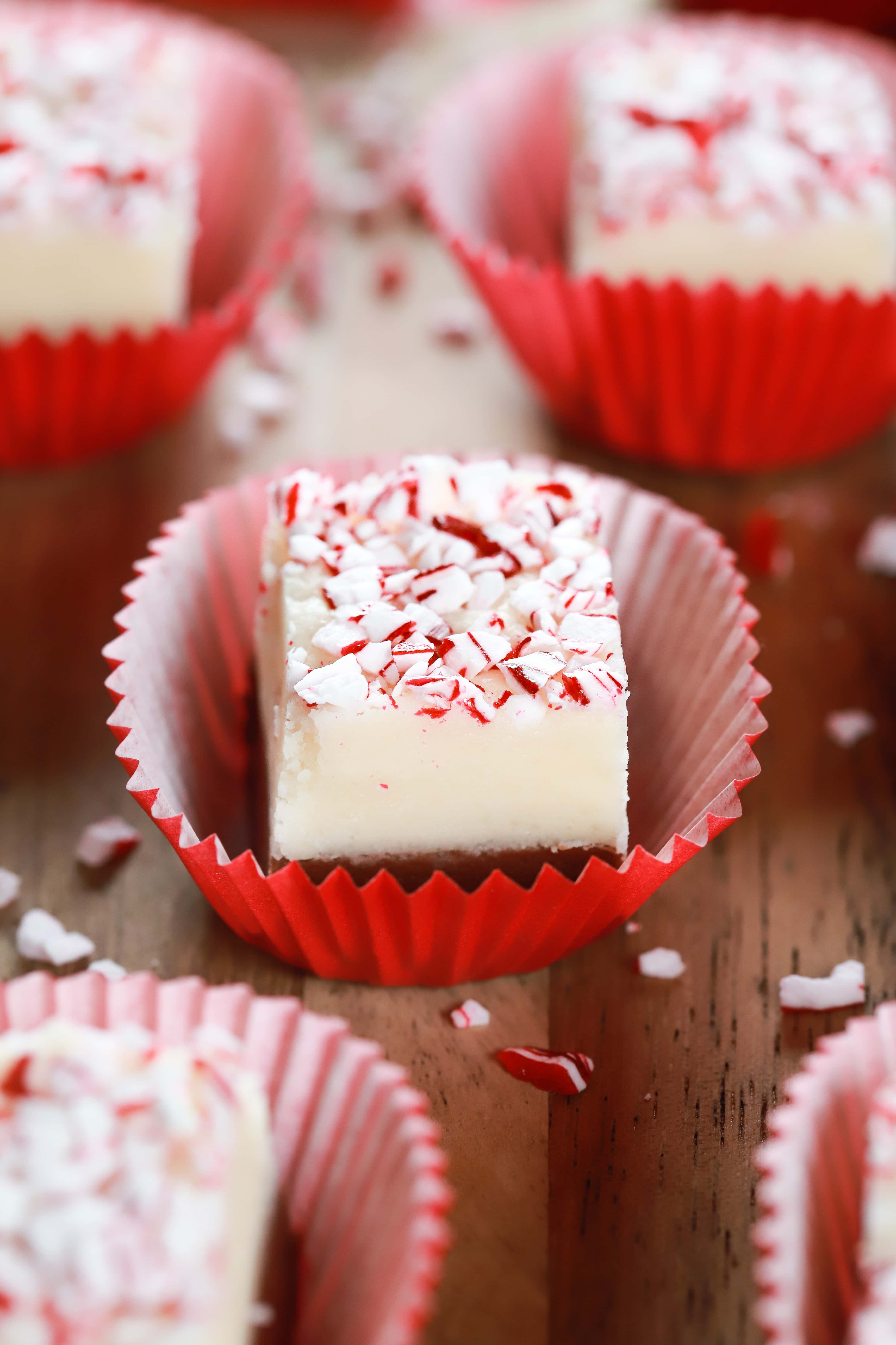 Layered chocolate peppermint fudge in a red cupcake liner surrounded by crushed peppermints. Recipe from A Kitchen Addiction