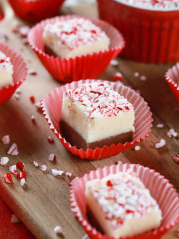 Up close image of a piece of chocolate peppermint layered fudge in a red cupcake liner on a wooden cutting board. Recipe from A Kitchen Addiction