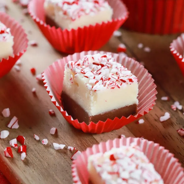 Up close image of a piece of chocolate peppermint layered fudge in a red cupcake liner on a wooden cutting board. Recipe from A Kitchen Addiction
