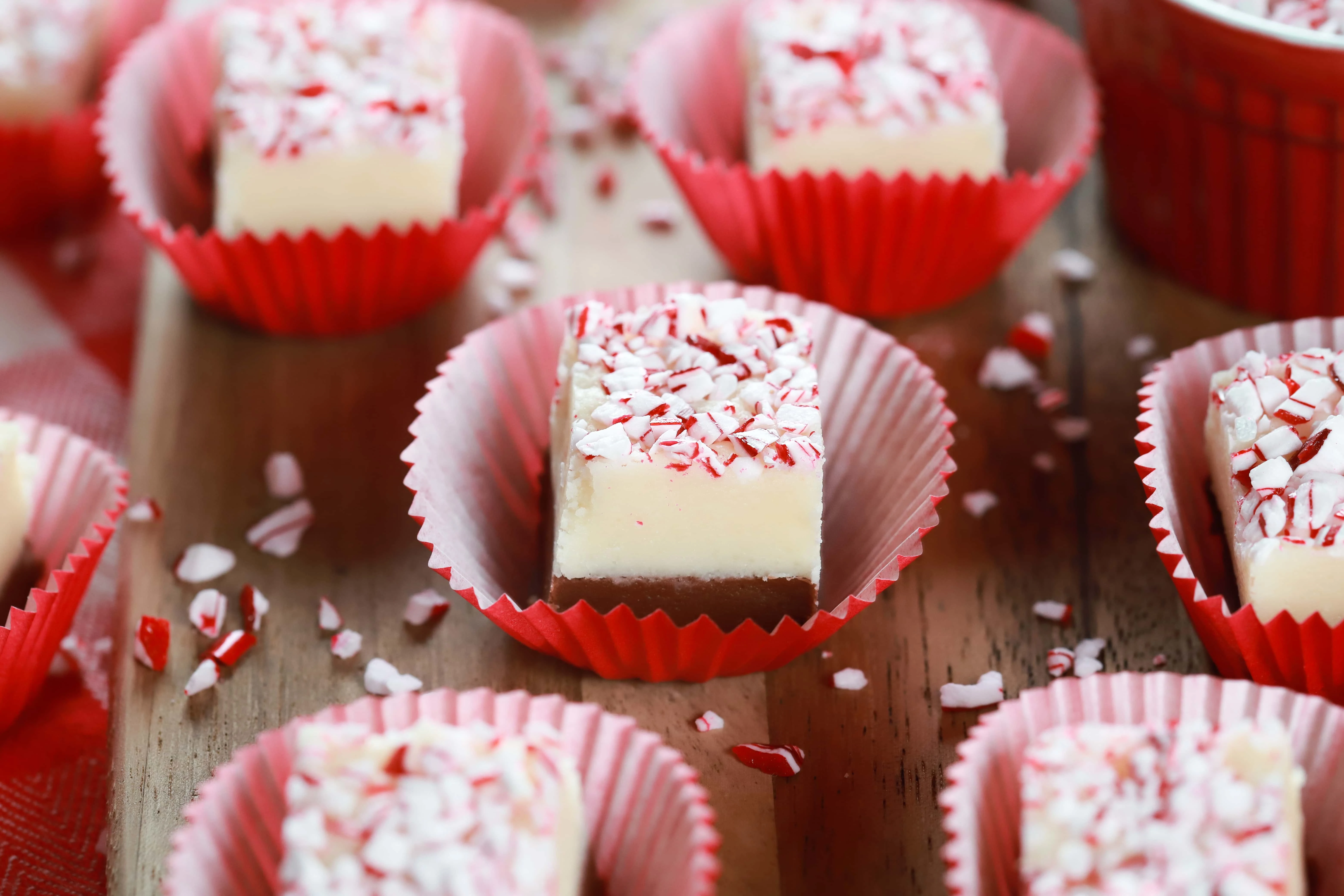 Pieces of chocolate peppermint layered fudge in red cup cake liners on a wooden cutting board. Recipe for fudge from A Kitchen Addiction