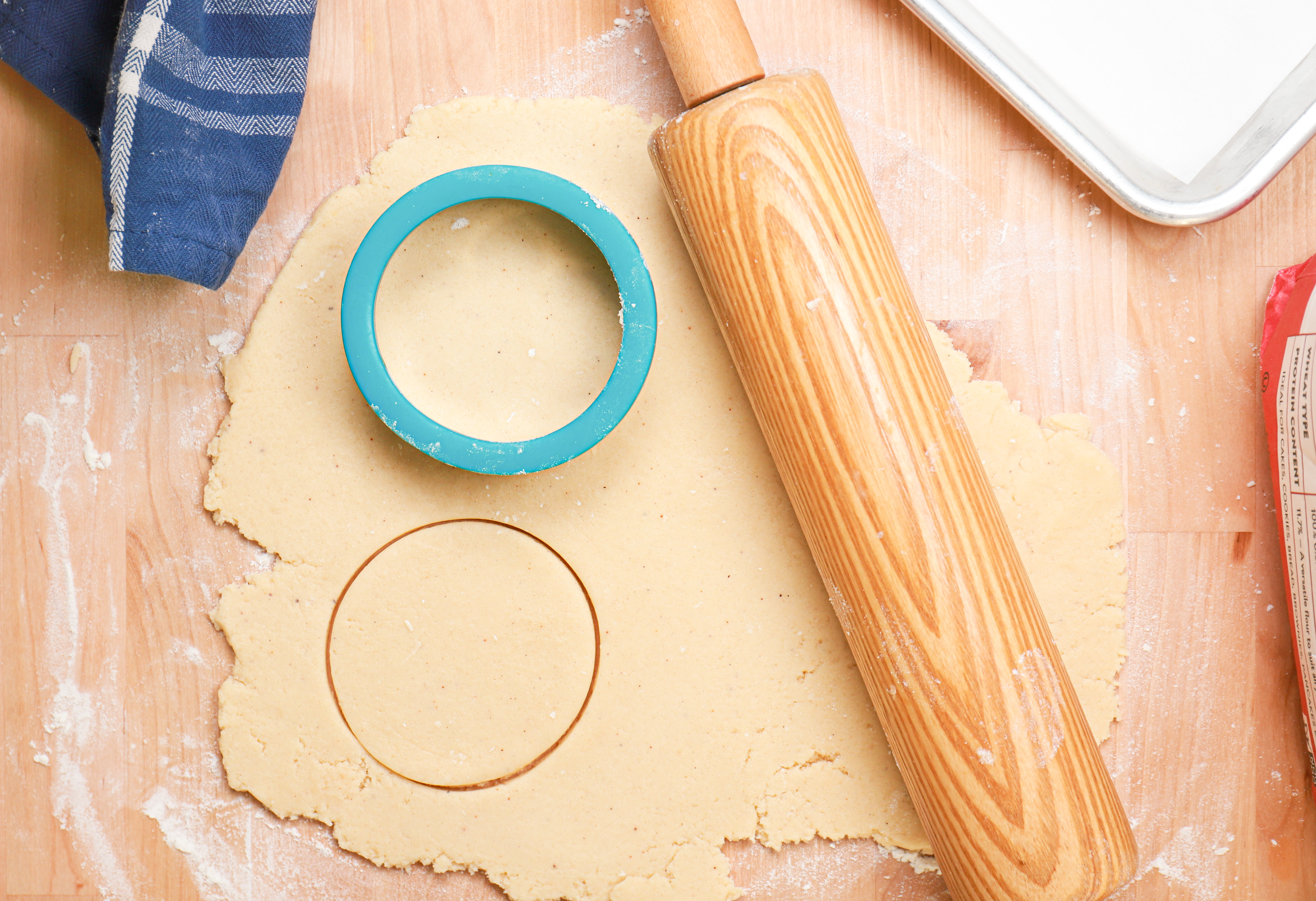 Sour cream cookie dough rolled out on a floured surface with a cookie cutter on the dough and a rolling pin off to the right side.