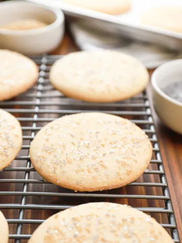 Up close view of an old fashioned sour cream cookie topped with sprinkles on a wire cooling rack with more cookies in the background.