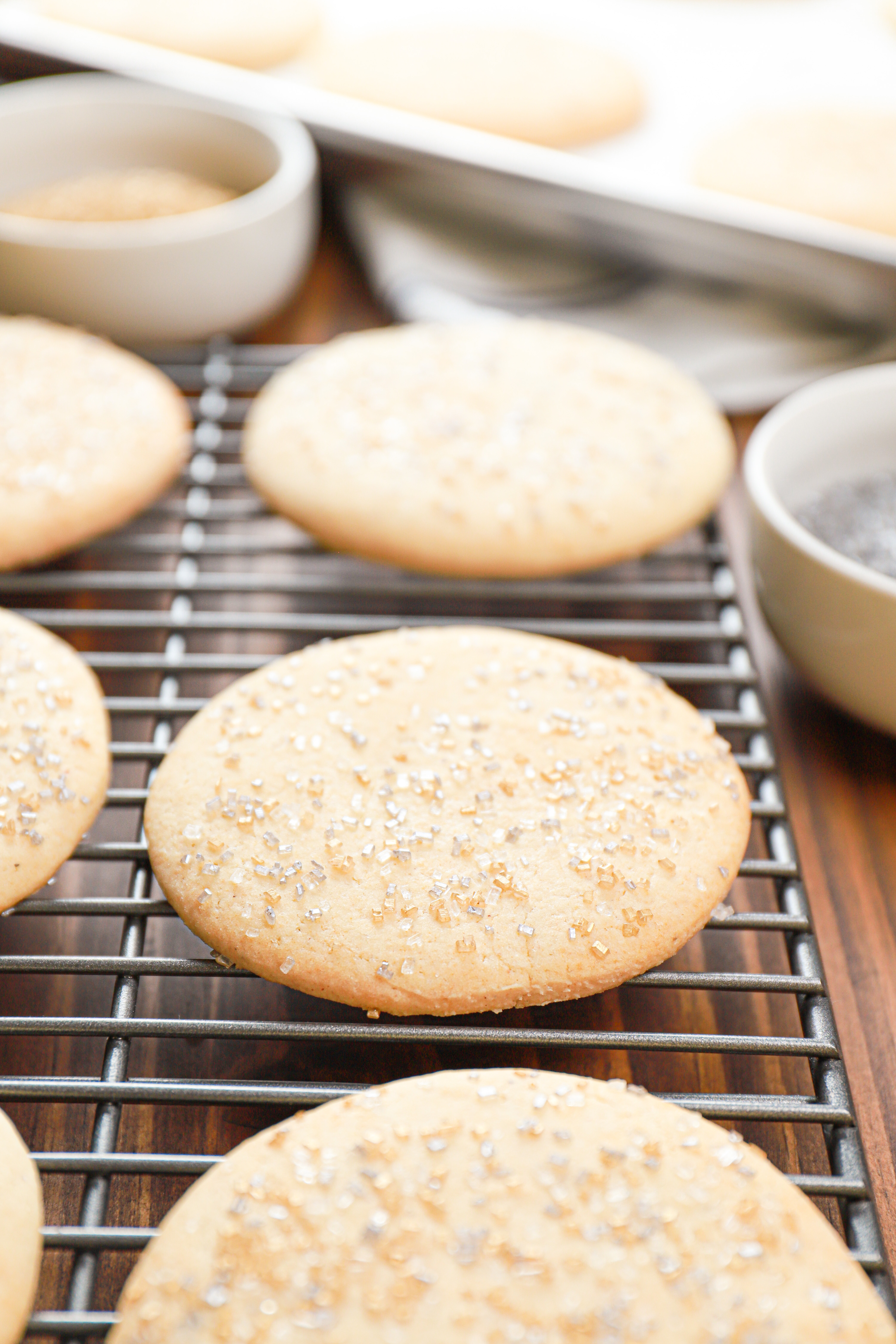 Up close view of an old fashioned sour cream cookie topped with sprinkles on a wire cooling rack with more cookies in the background.