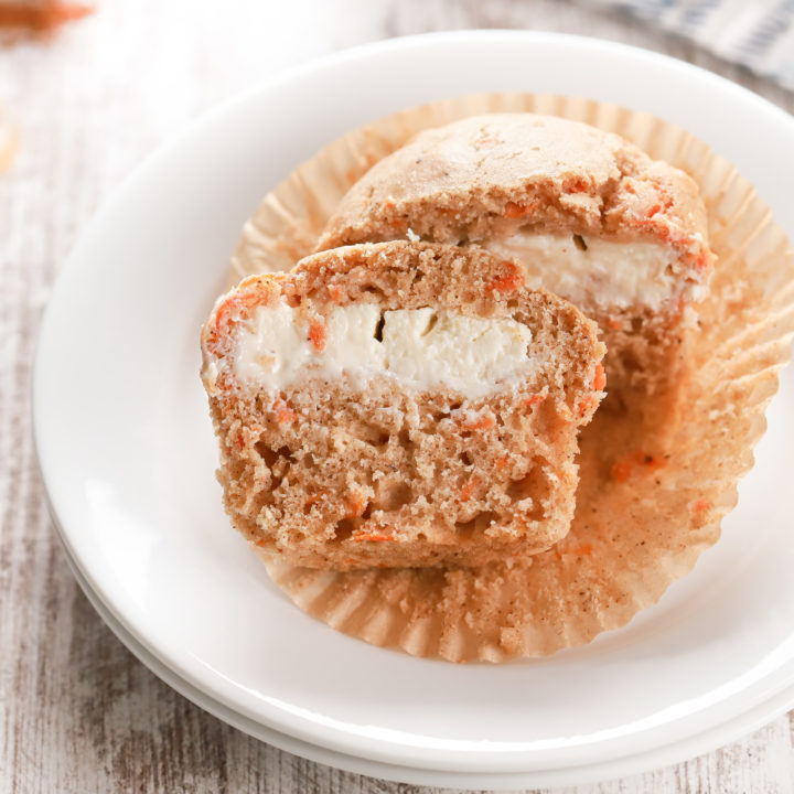 Side view of a carrot cake muffin on a small white plate sliced in half to show the cream cheese filling.