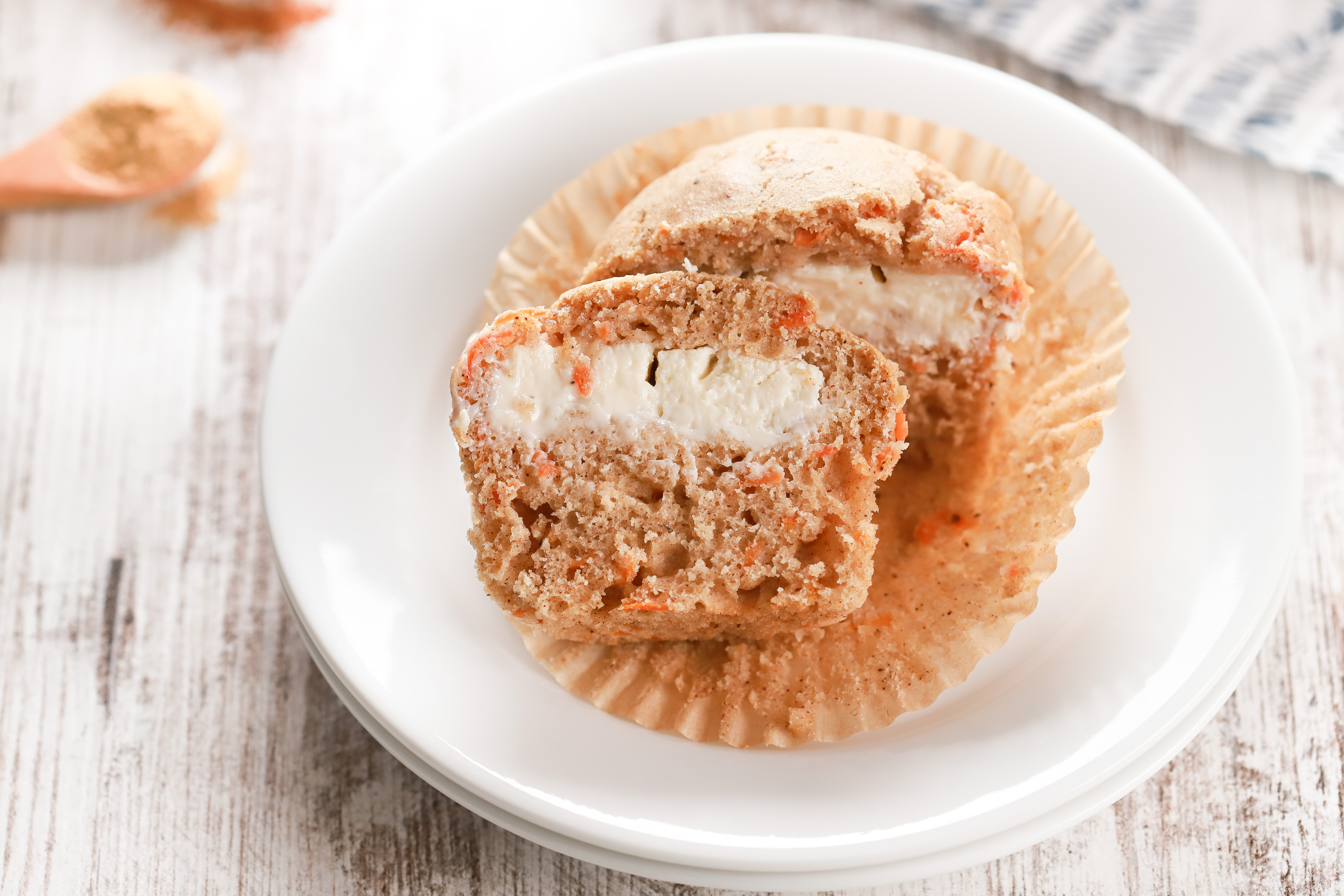 Side view of a carrot cake muffin on a small white plate sliced in half to show the cream cheese filling.