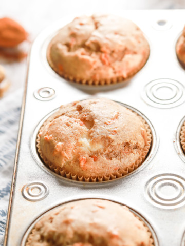 Up close side view of a cream cheese filled carrot cake muffin in an aluminum muffin tin.