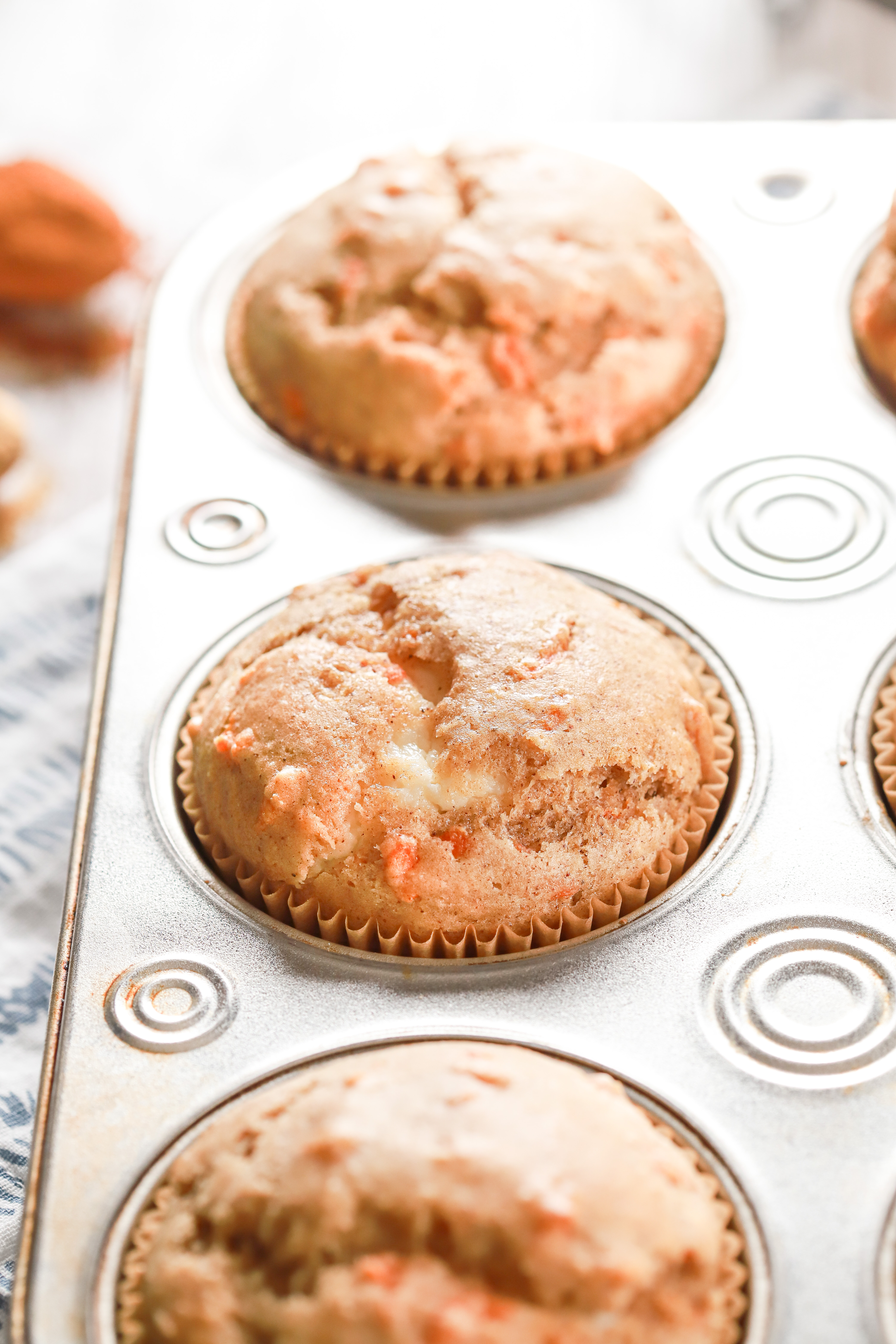 Up close side view of a cream cheese filled carrot cake muffin in an aluminum muffin tin.