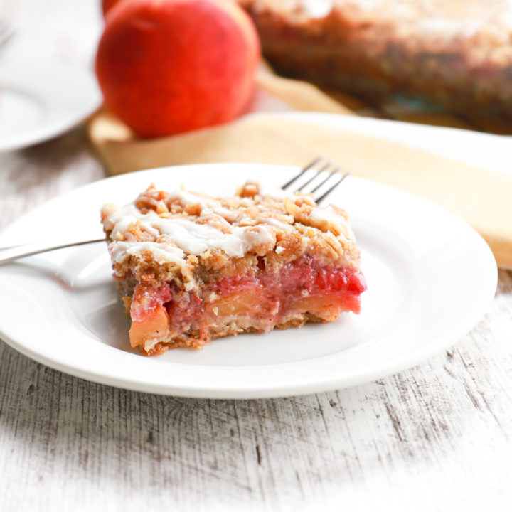 Up close side view of a strawberry peach streusel bar on a small white plate.