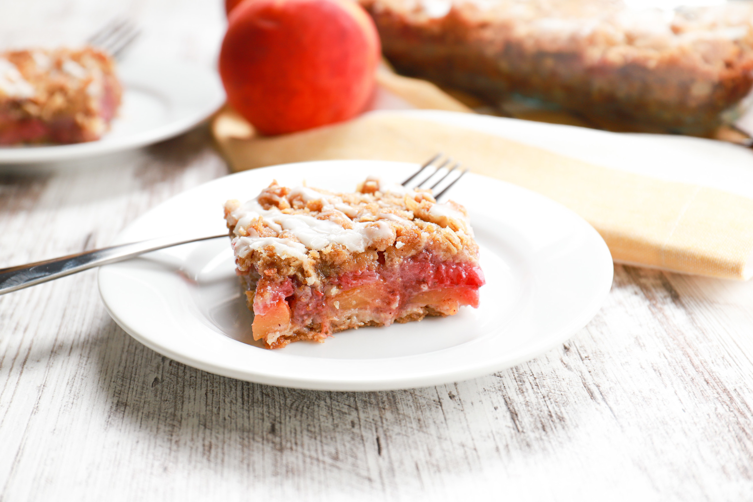 Up close side view of a strawberry peach streusel bar on a small white plate.