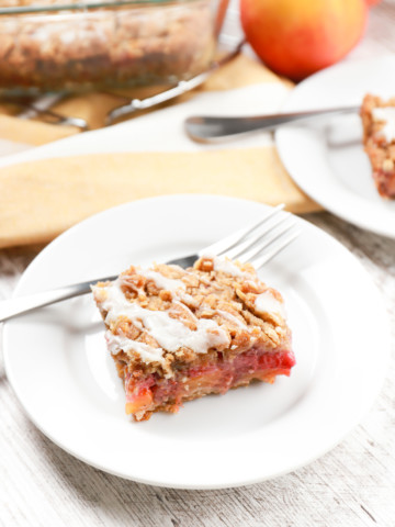 A strawberry peach streusel bar on a small white plate with the pan of remaining bars in the background.