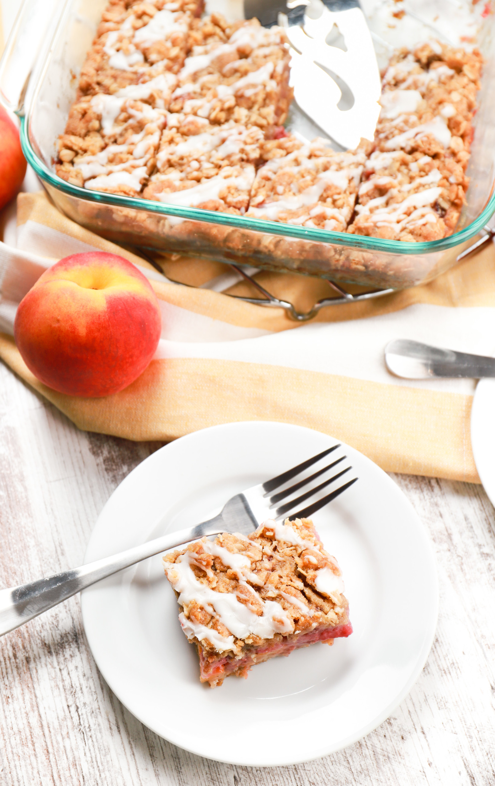 Overhead view of a pan of strawberry peach streusel bars and a small white plate with one streusel bar.