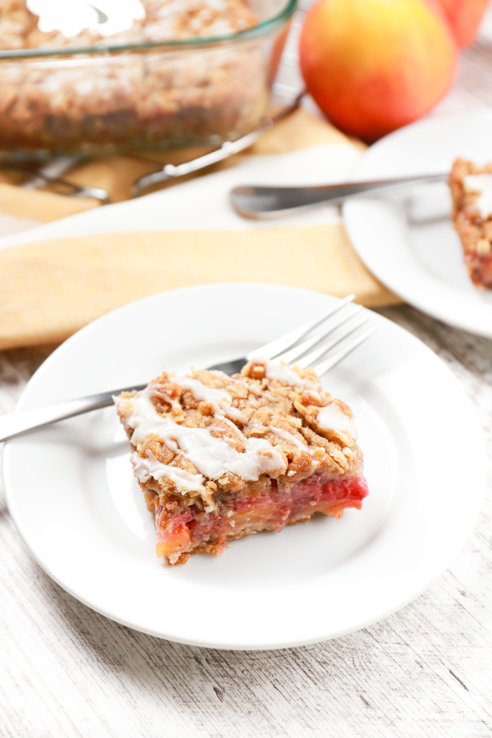 A strawberry peach streusel bar on a small white plate with the pan of remaining bars in the background.