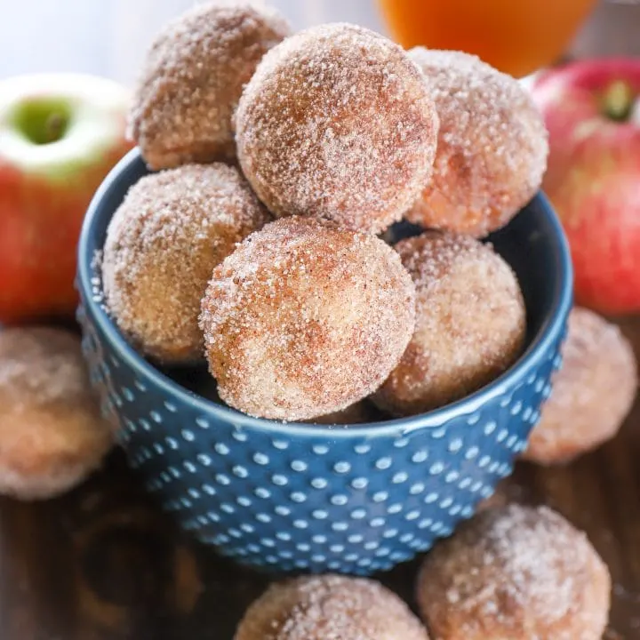 Bowl of Mini Spiced Apple Cider Donut Muffins with apples and a mug of apple cider. Recipe from A Kitchen Addiction