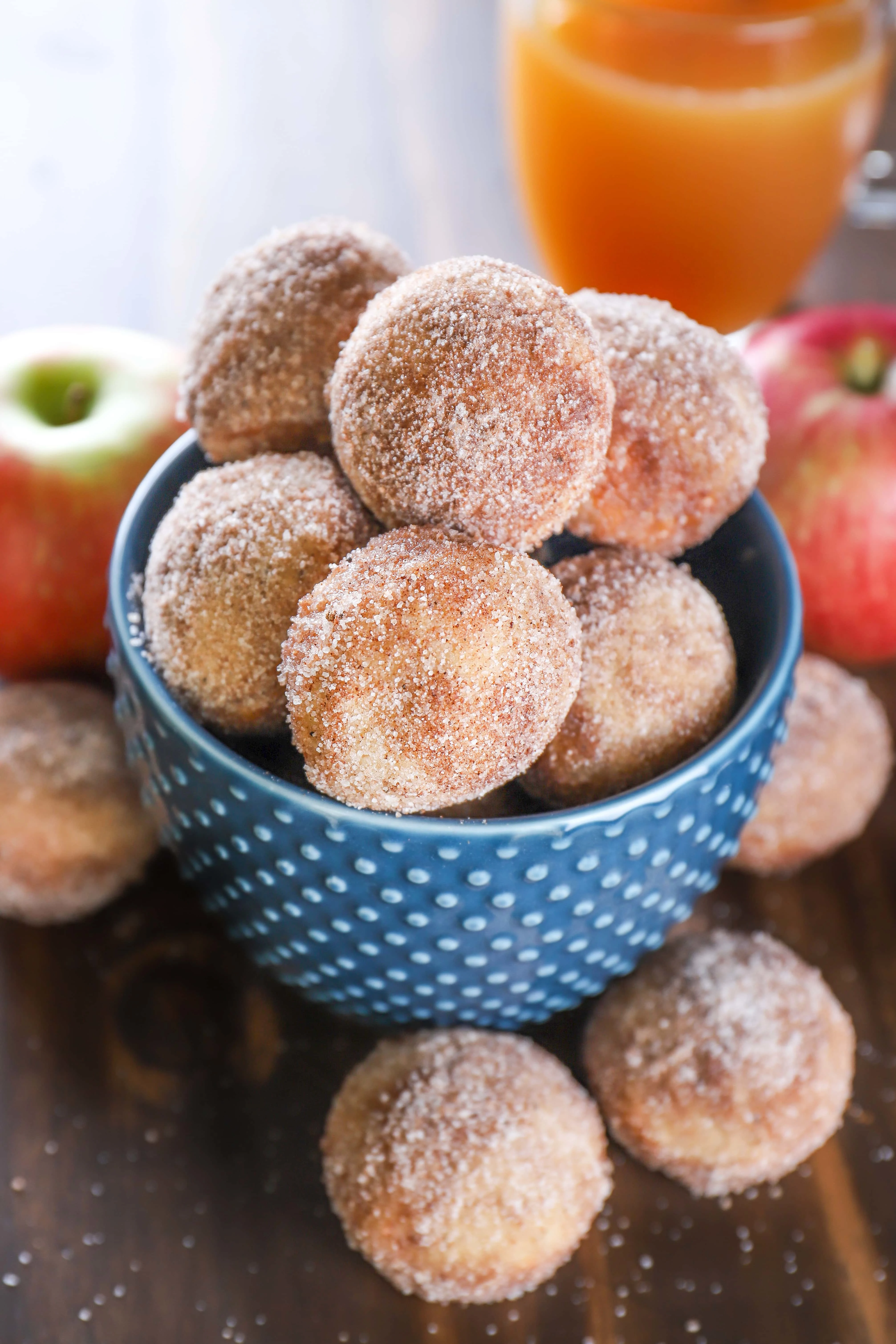 Bowl of Mini Spiced Apple Cider Donut Muffins with apples and a mug of apple cider. Recipe from A Kitchen Addiction
