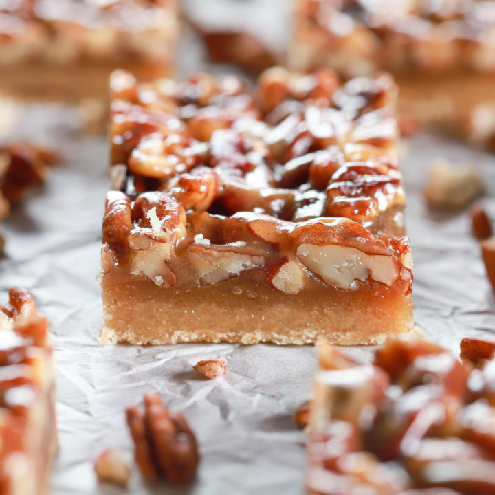 Side view of a honey pecan pie bar with more bars in the background on a piece of white parchment paper
