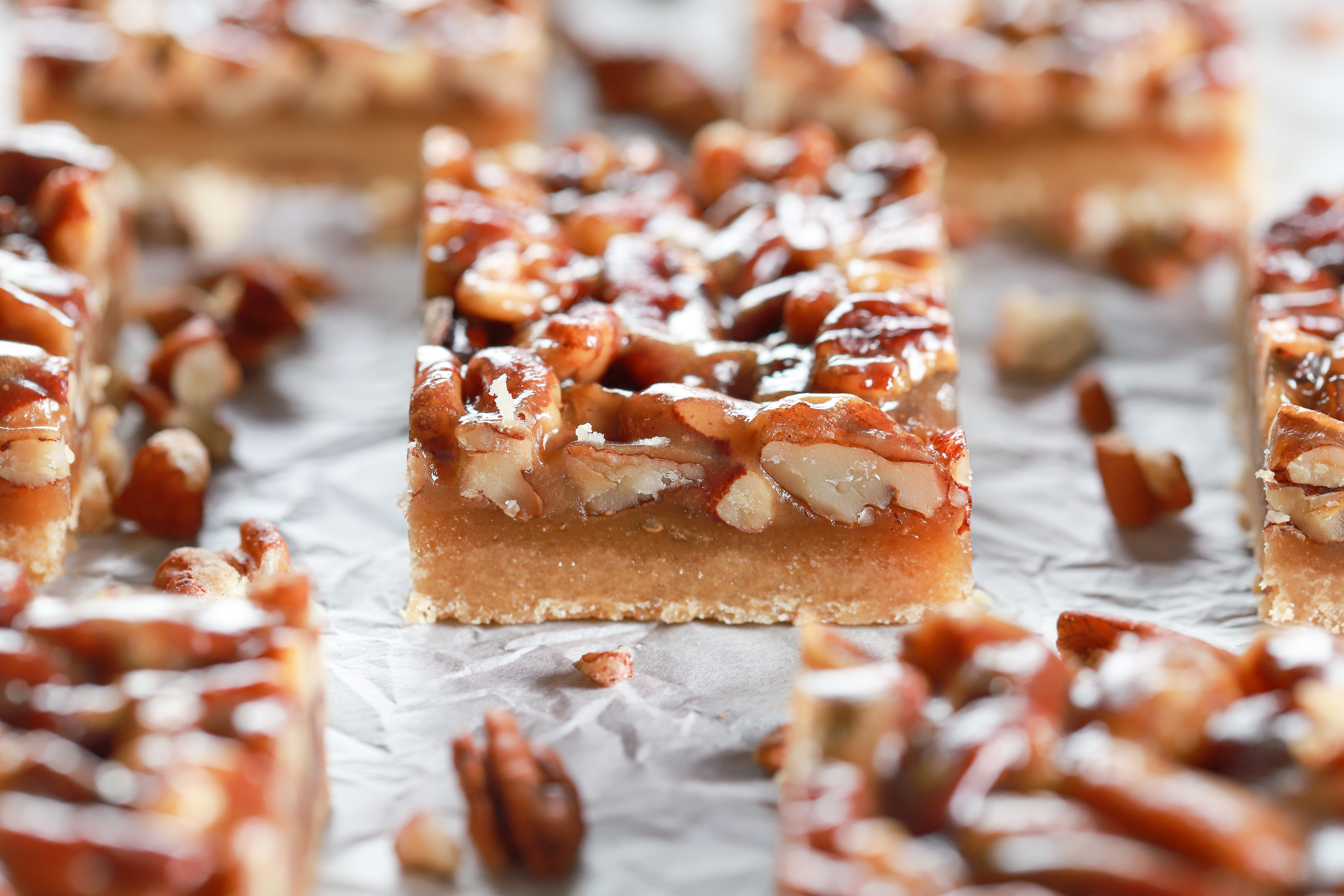 Side view of a honey pecan pie bar with more bars in the background on a piece of white parchment paper