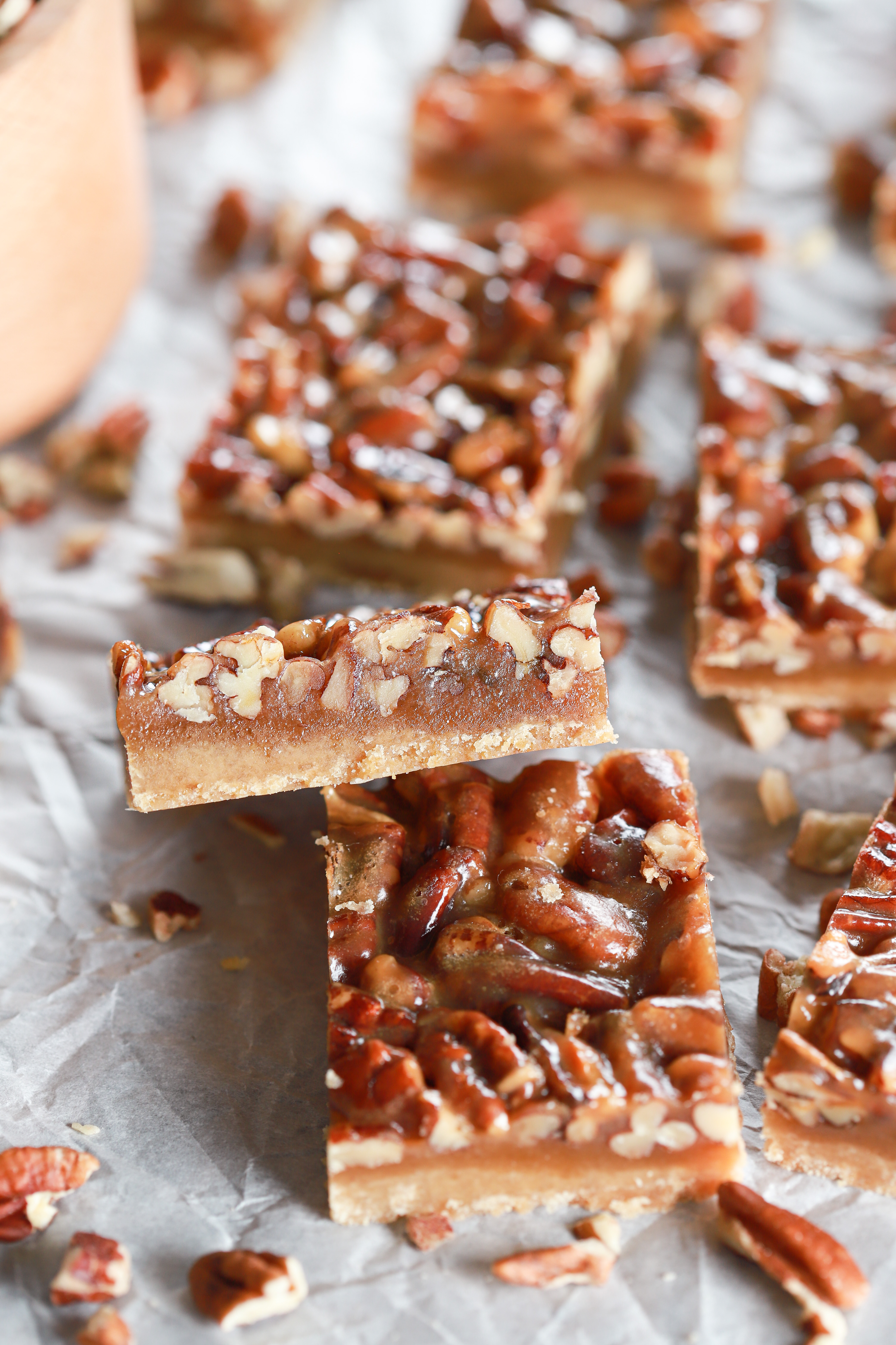Up close side view of a honey pecan pie bar on a piece of parchment paper