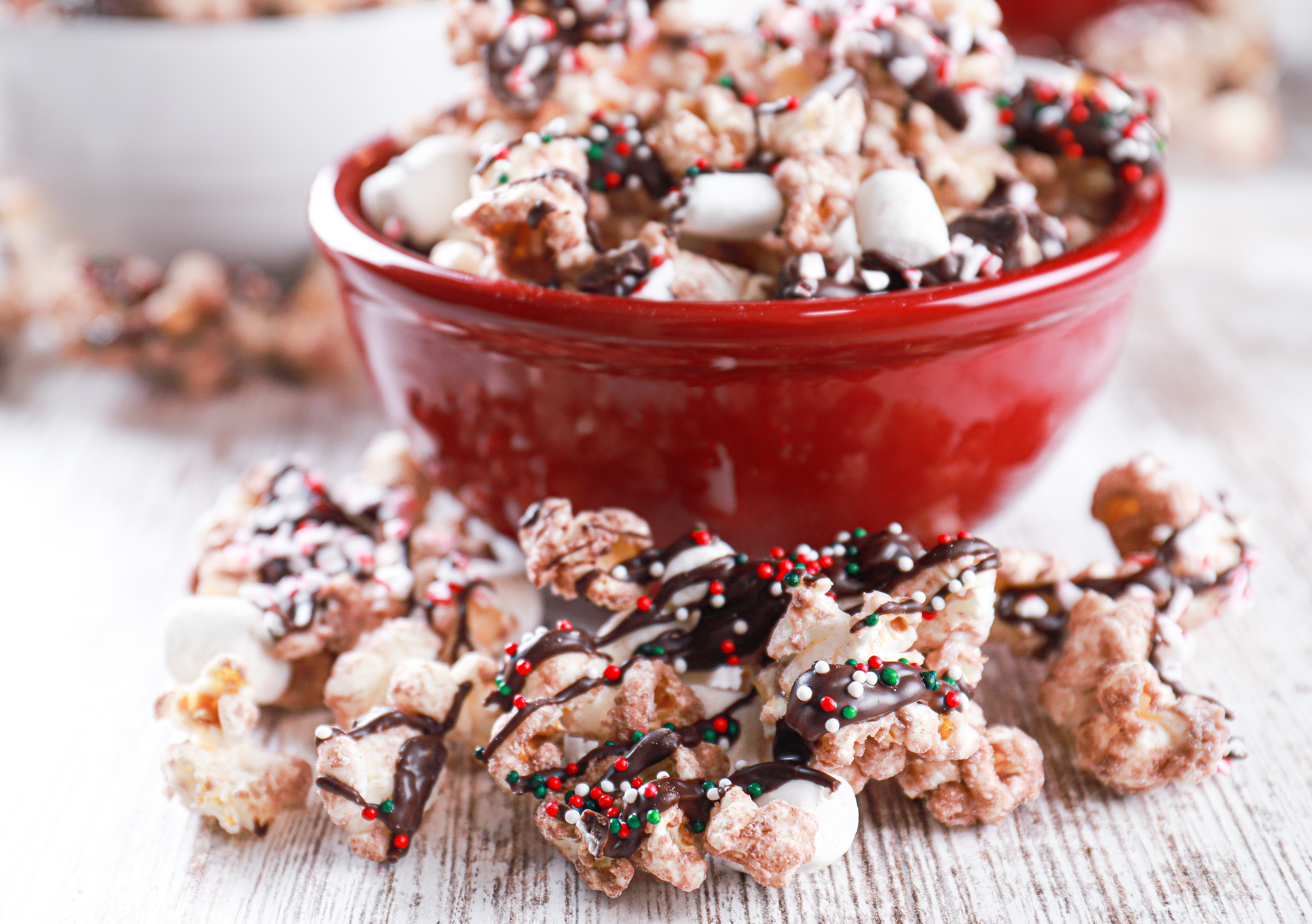 Up close view of chocolate drizzled hot chocolate popcorn on a white board in front of a red bowl filled with popcorn.