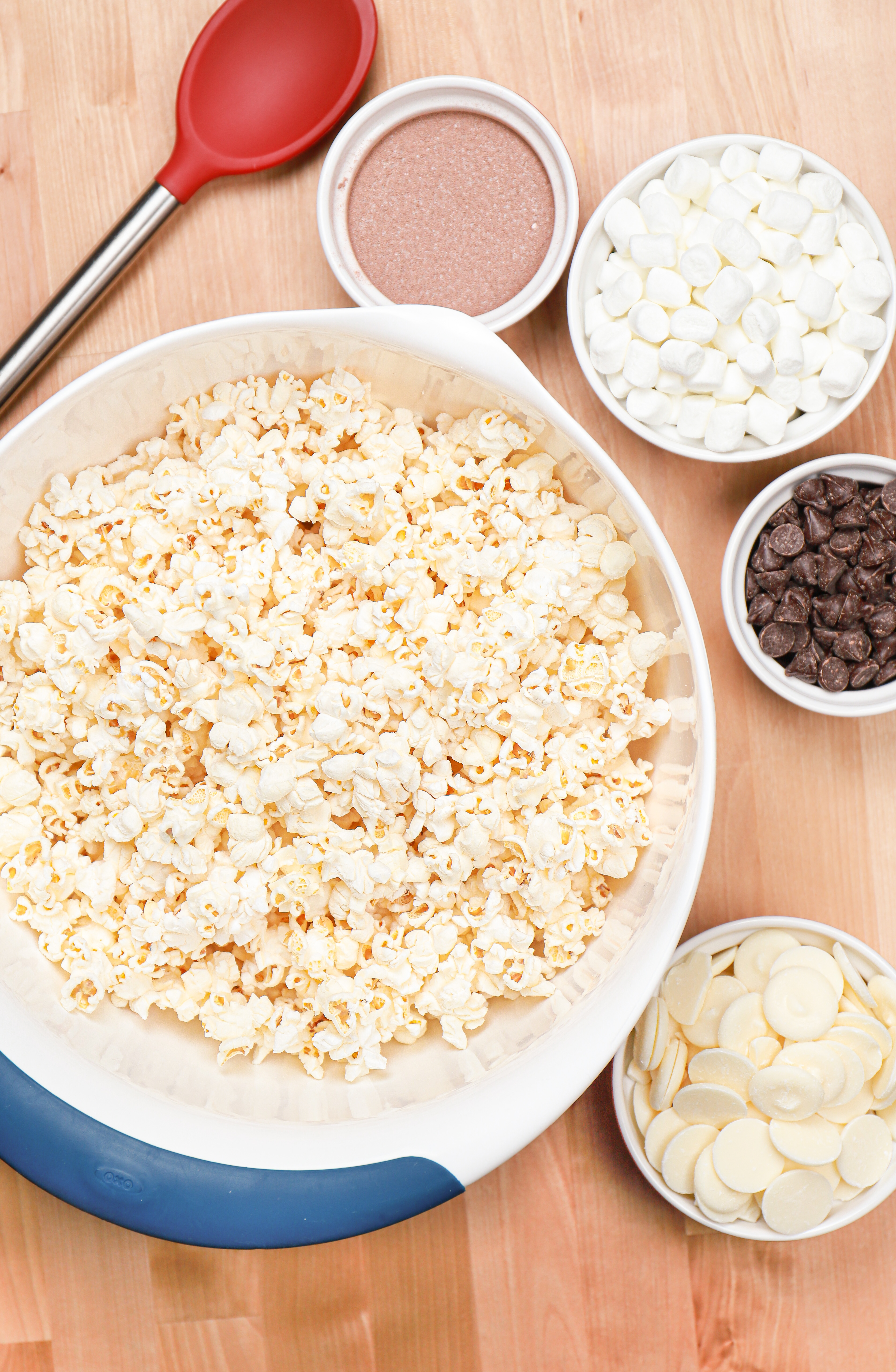 Overhead view of popcorn, hot chocolate mix, chocolate chips, mini marshmallows, and candy melts. These are the ingredients needed to make hot chocolate popcorn.