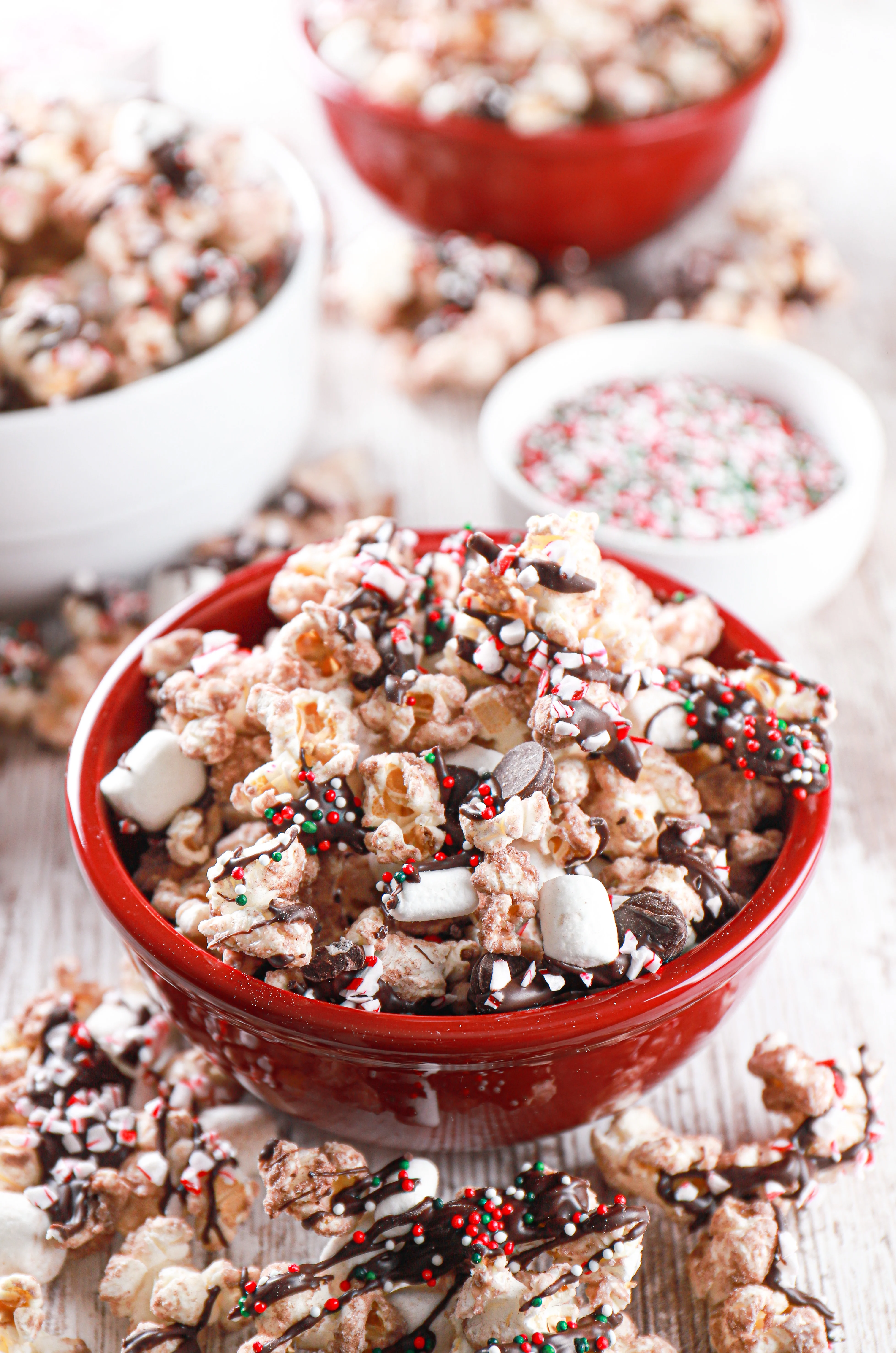 Hot chocolate popcorn in a small red bowl with another red bowl and white bowl full of popcorn in the background. Recipe for popcorn from A Kitchen Addiction.