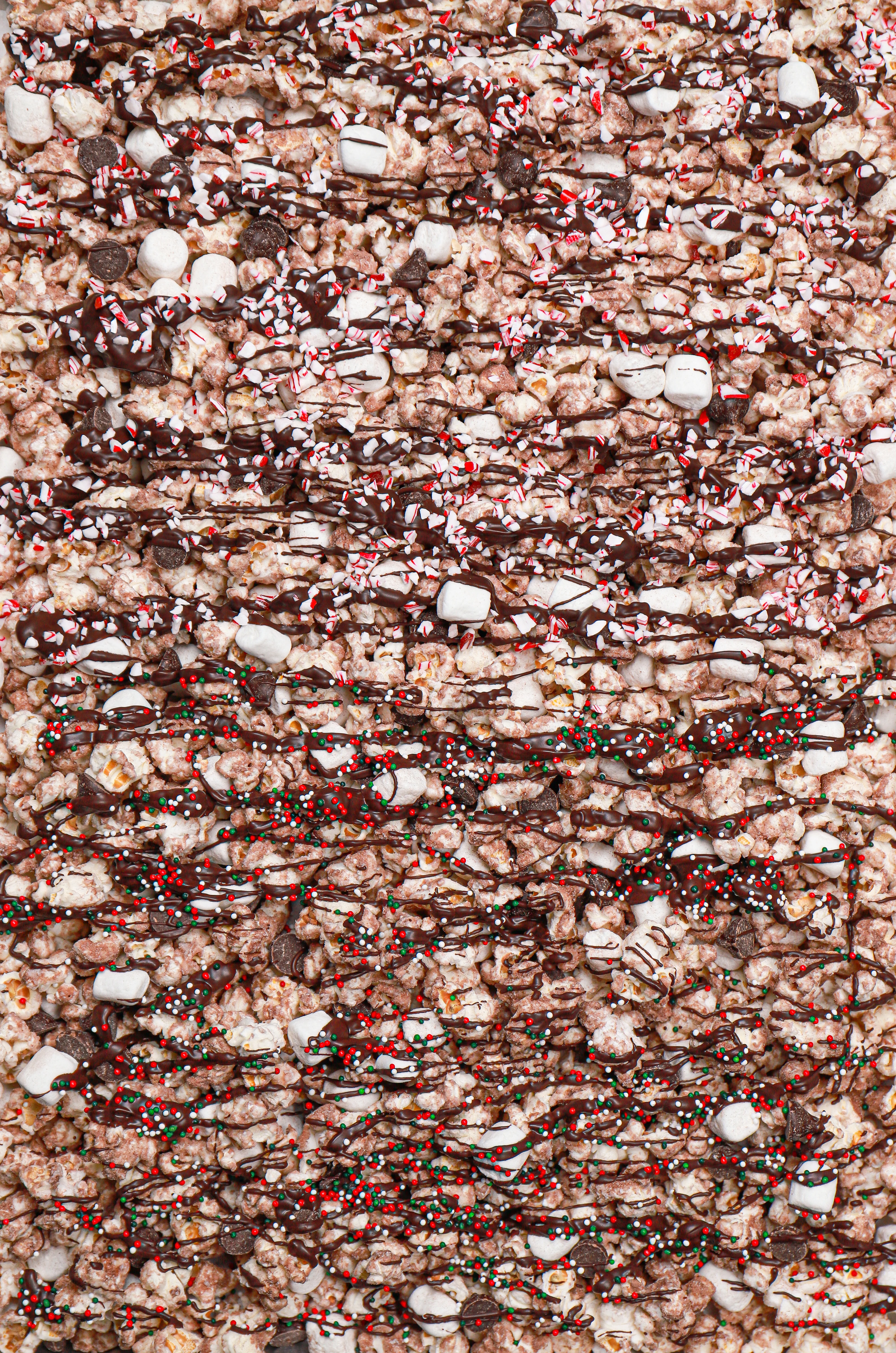 Overhead view of a batch of hot chocolate popcorn with toppings on a rimmed baking sheet.