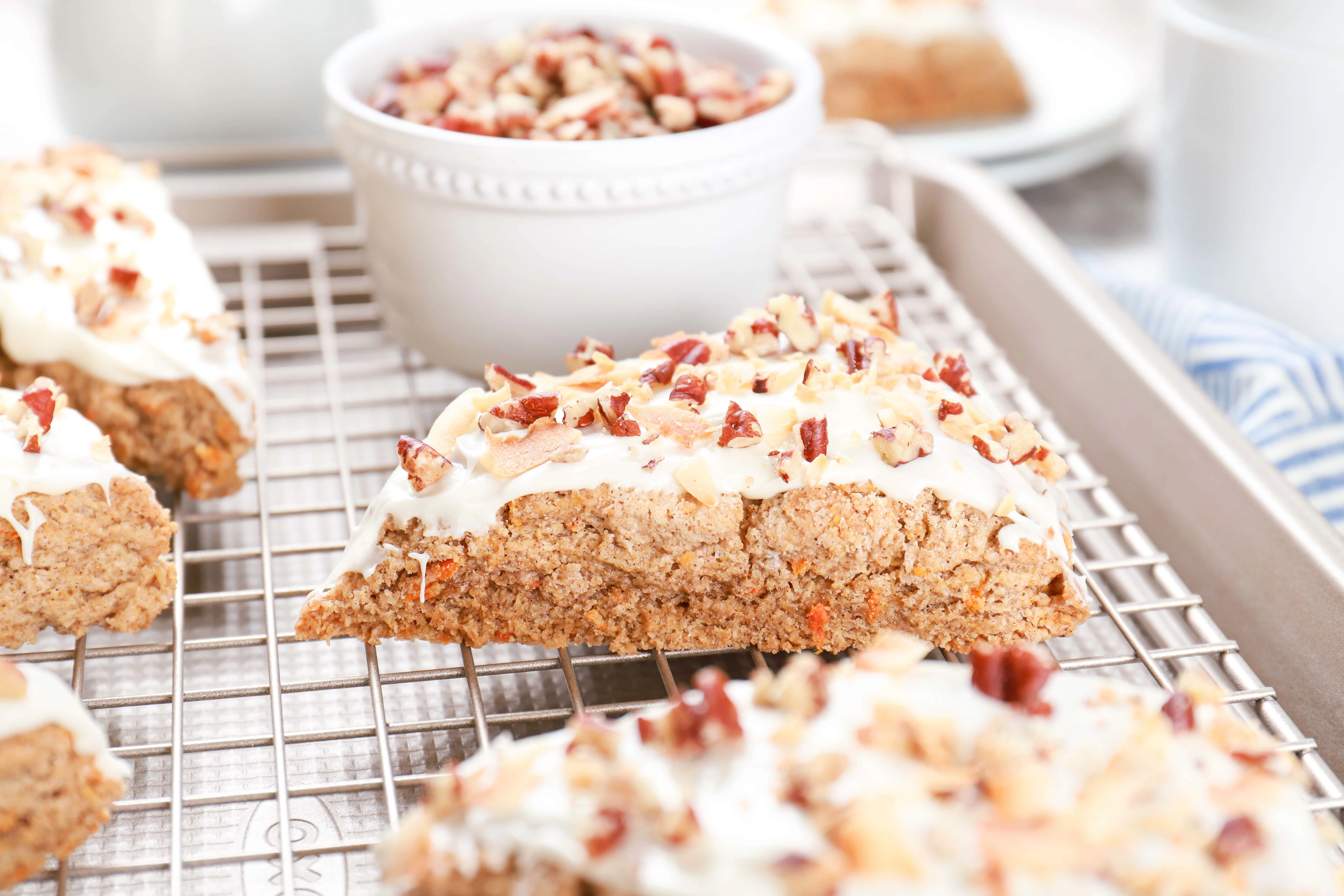 Carrot cake scone on a cooling rack with a bowl of chopped pecans in the background. Recipe for scones from A Kitchen Addiction