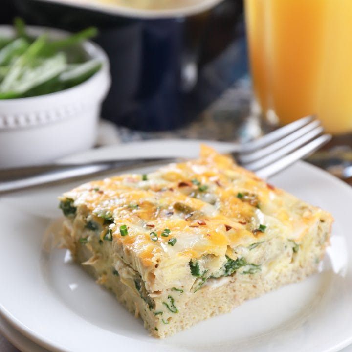 Piece of cheesy spinach artichoke egg bake on a white plate. Recipe for egg bake from A Kitchen Addiction