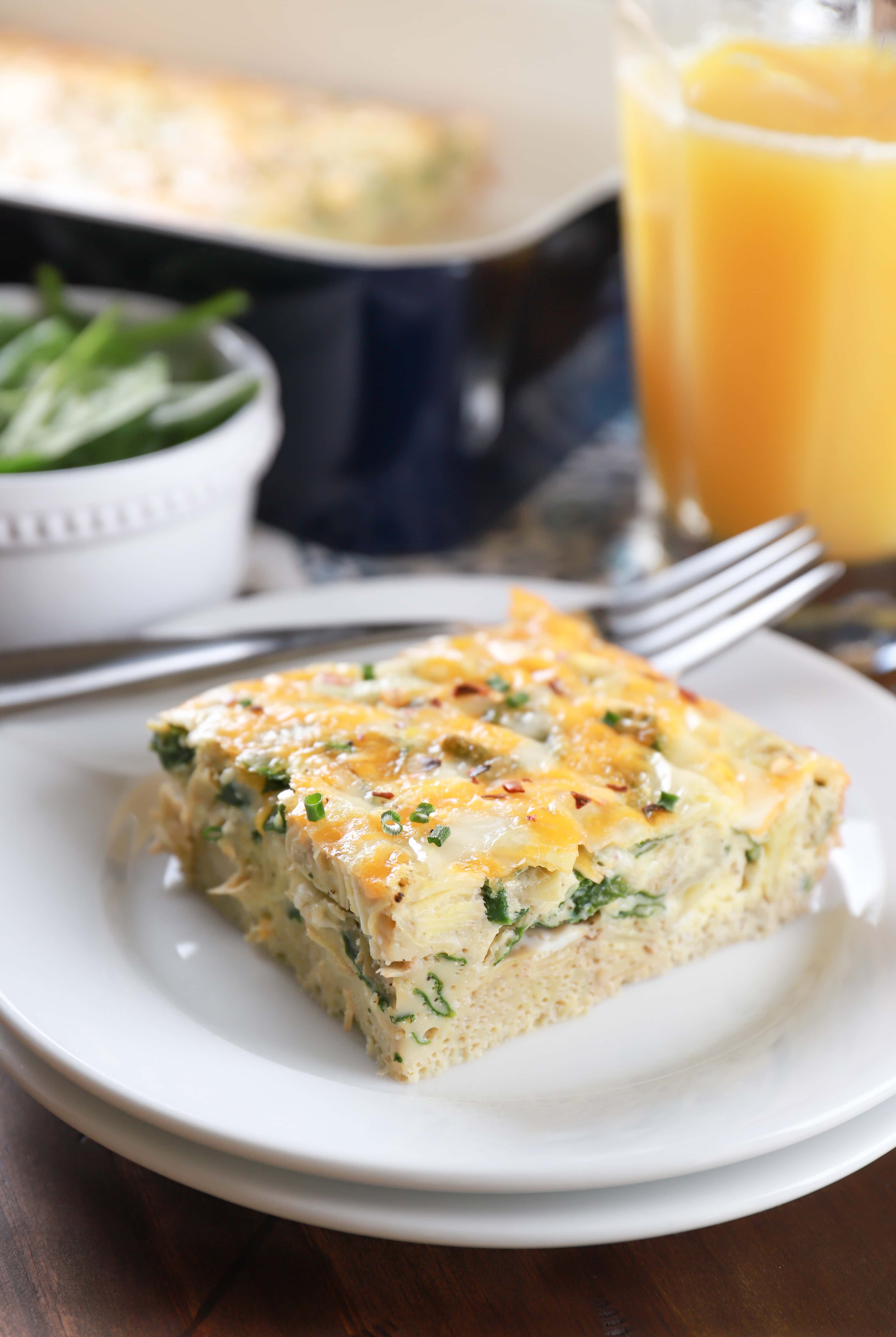 Piece of cheesy spinach artichoke egg bake on a white plate. Recipe for egg bake from A Kitchen Addiction