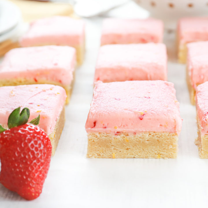 Up close side view of a strawberry lemon buttercream frosted sugar cookie bar on a piece of parchment paper.