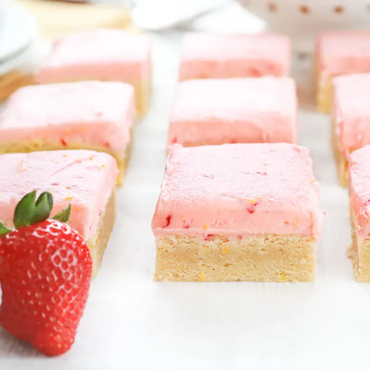 Up close side view of a strawberry lemon buttercream frosted sugar cookie bar on a piece of parchment paper.