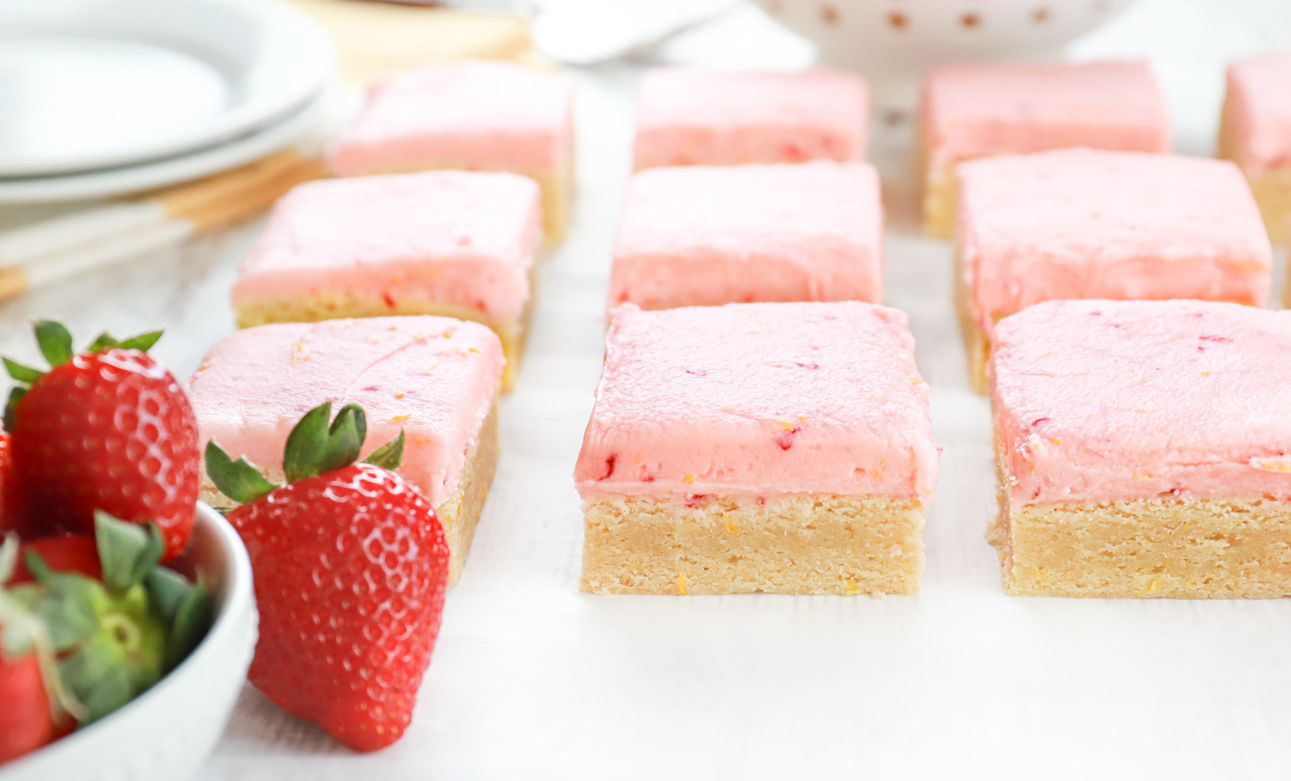 Up close side view of a strawberry lemon buttercream frosted sugar cookie bar on a piece of parchment paper.