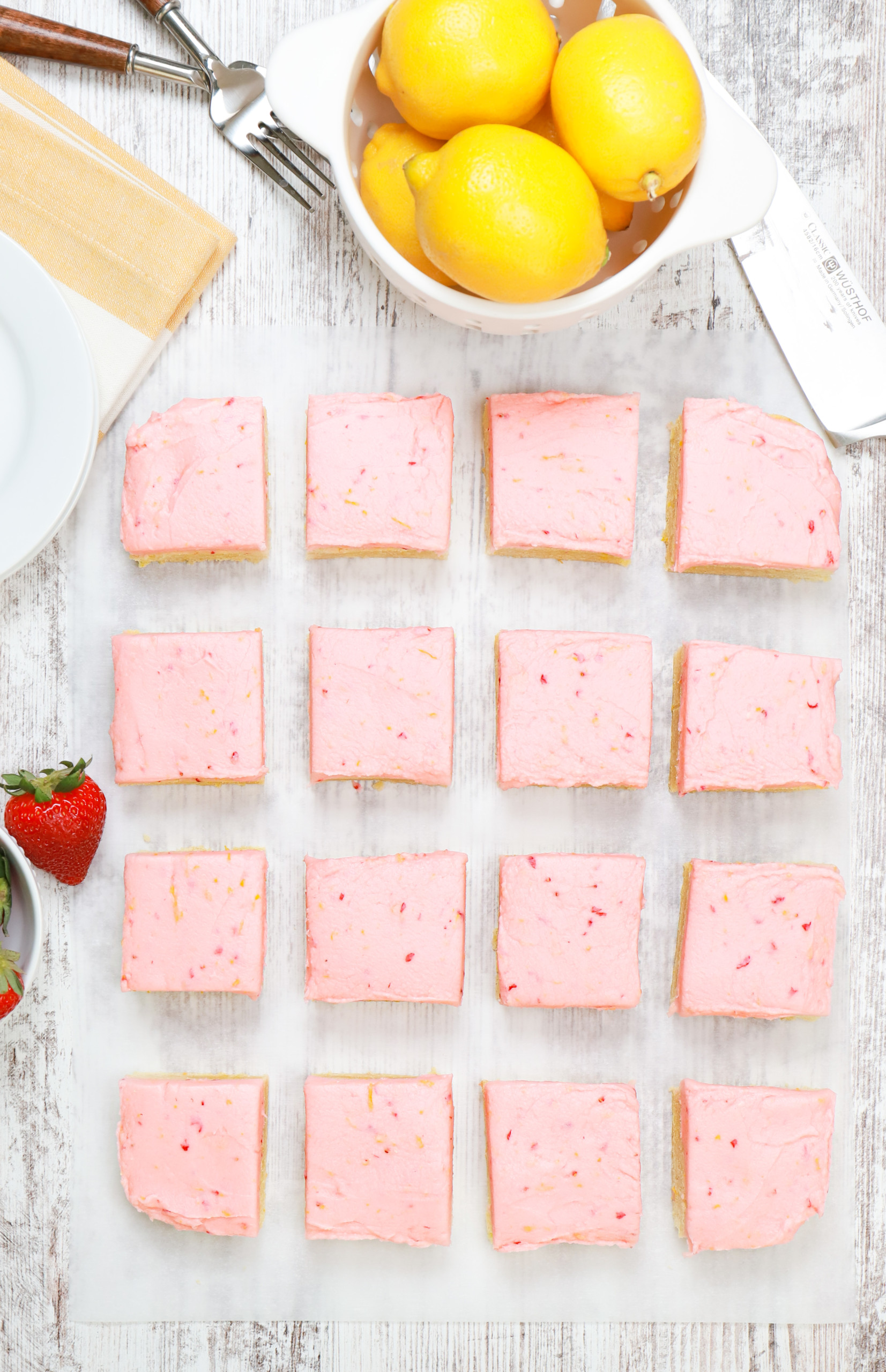 Overhead view of a batch of strawberry lemon buttercream frosted sugar cookie bars cut into pieces on a piece of parchment paper.