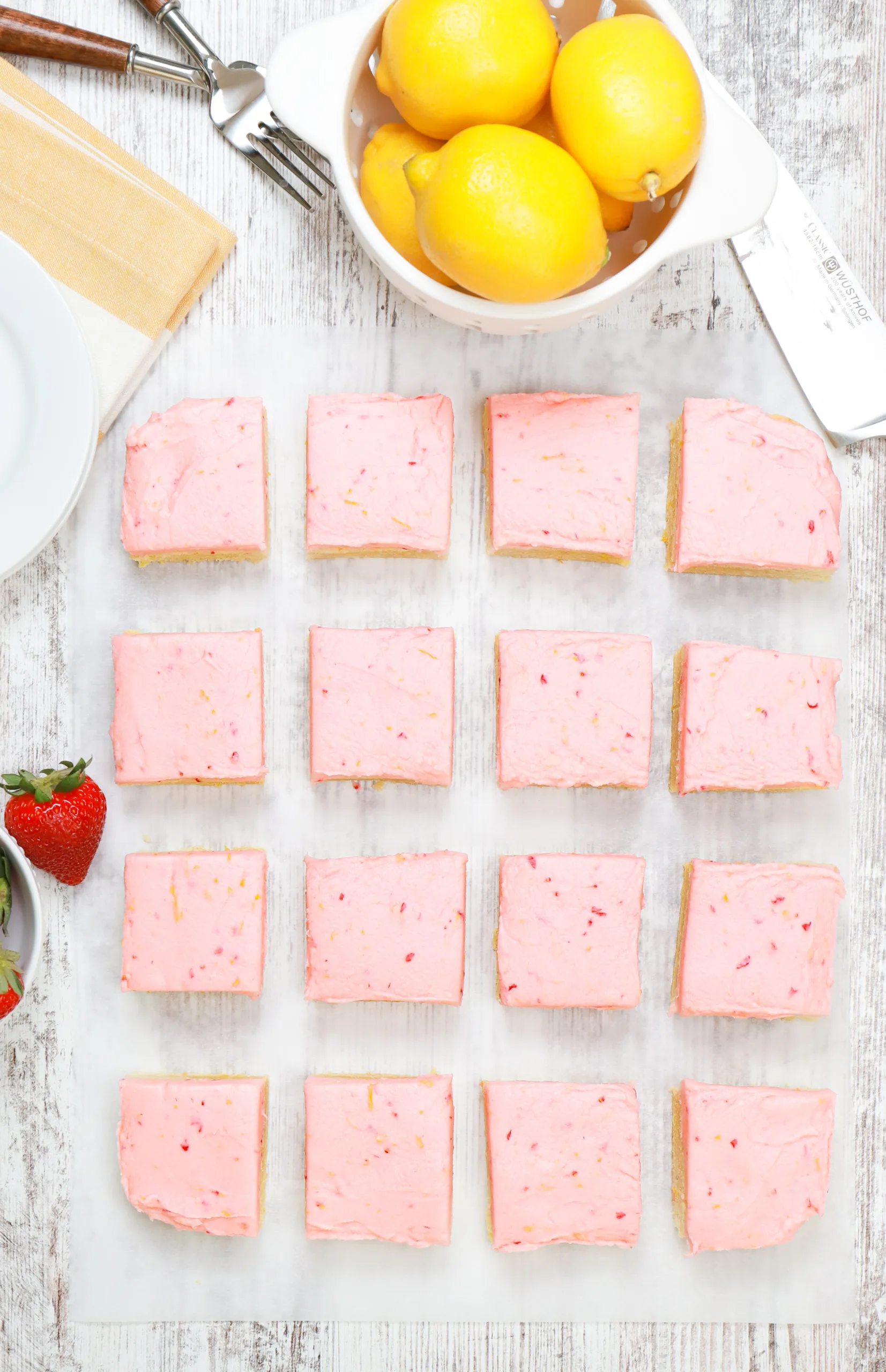 Overhead view of a batch of strawberry lemon buttercream frosted sugar cookie bars cut into pieces on a piece of parchment paper.