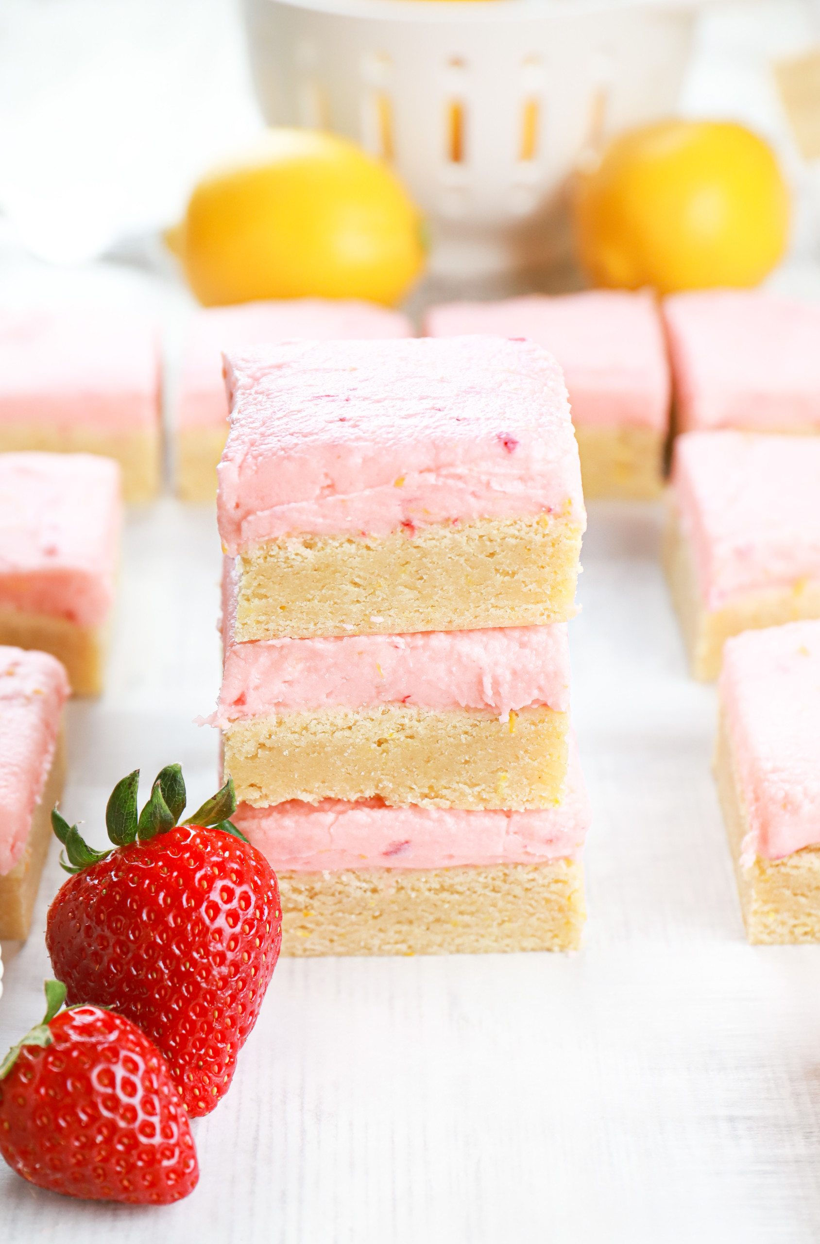 Three strawberry lemon frosted sugar cookie bars stacked on a piece of parchment paper.