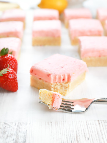 Fork with a piece of strawberry lemon frosted sugar cookie bar on it with the remainder of the bar in the background.