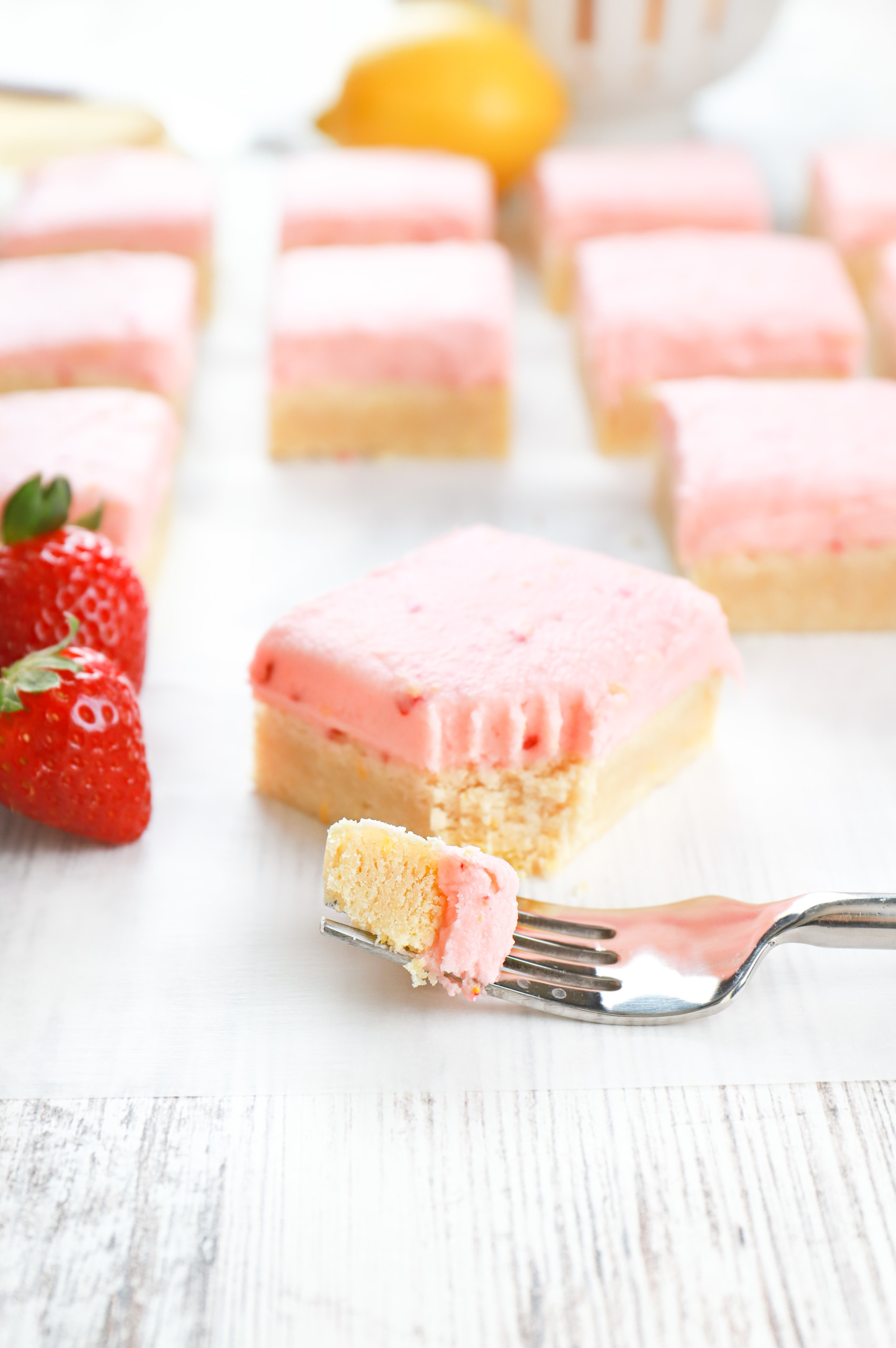 Fork with a piece of strawberry lemon frosted sugar cookie bar on it with the remainder of the bar in the background.