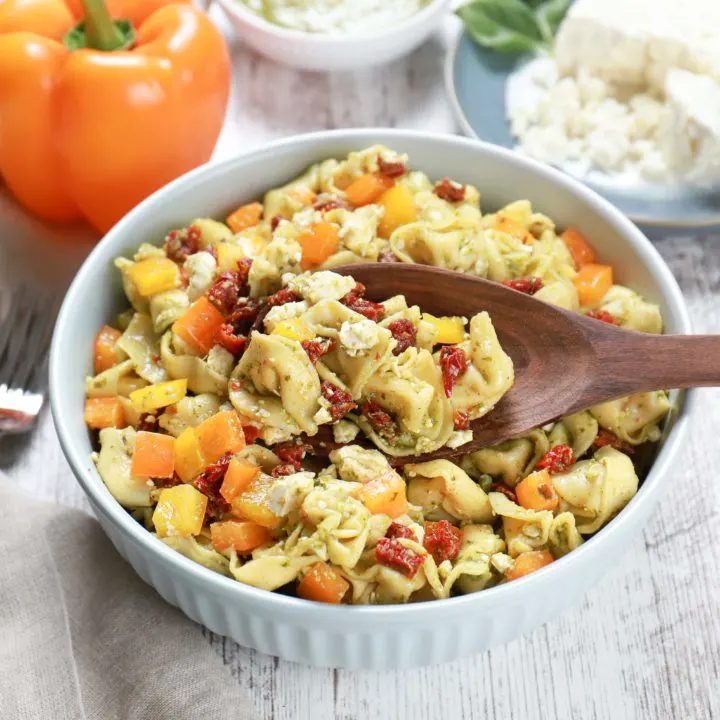 Above view of a wooden spoon full of pesto tortellini pasta salad.