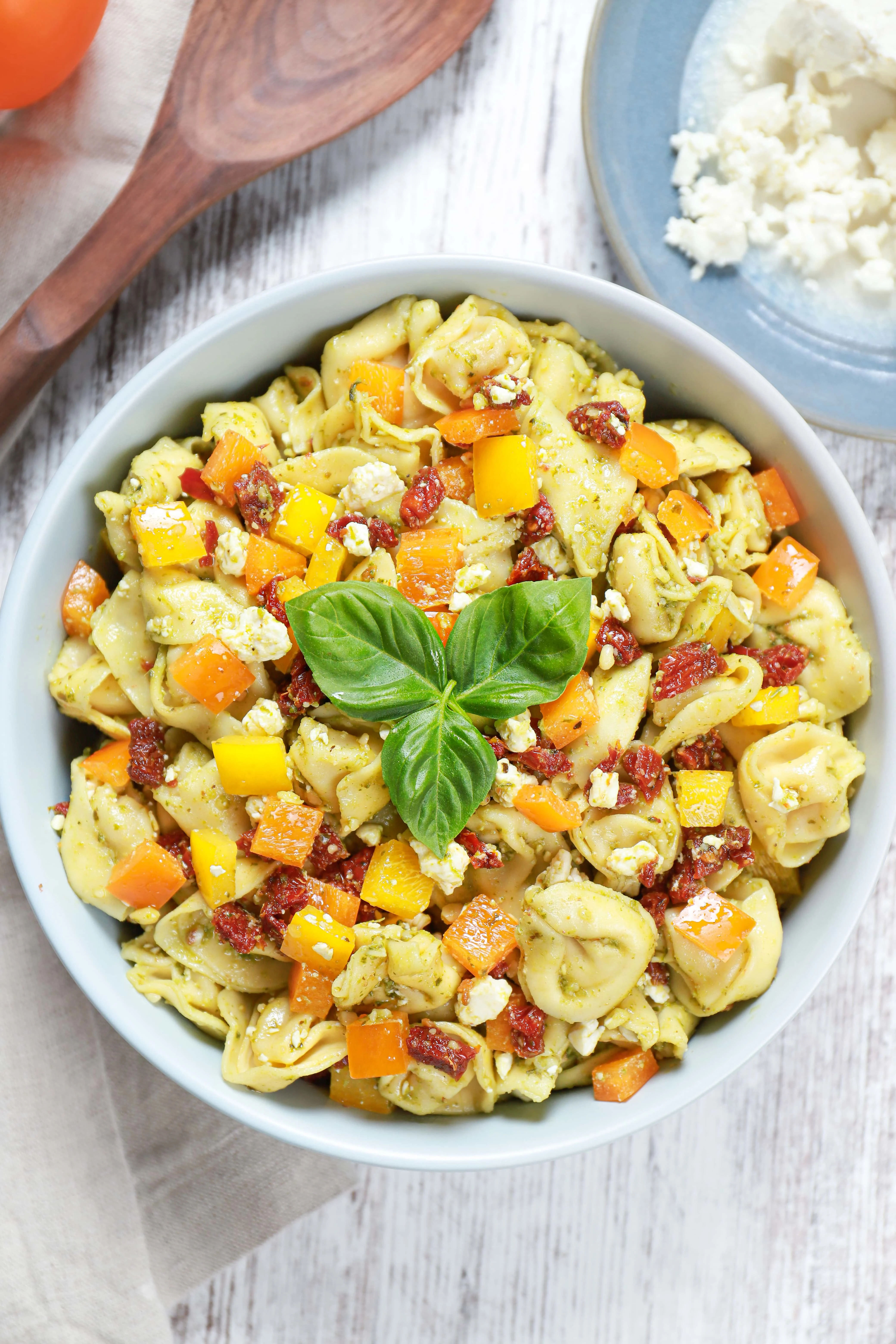 Above view of a bowl of Pesto Tortellini Salad garnished with basil leaves. Recipe from A Kitchen Addiction