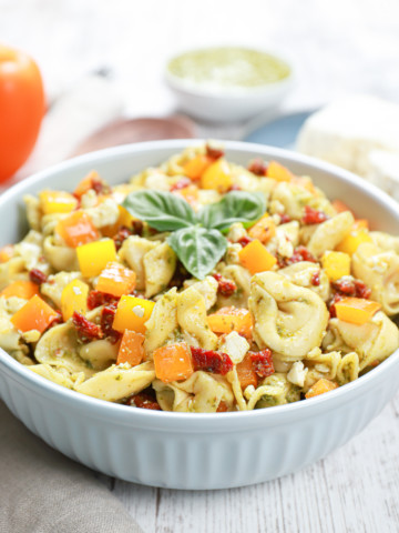 Side view of a blue bowl filled with pesto pasta salad.