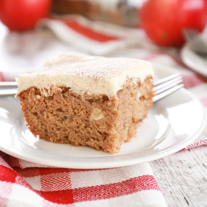 Up close view of a piece of apple cake on a small white plate with baking dish of remaining cake in the background.