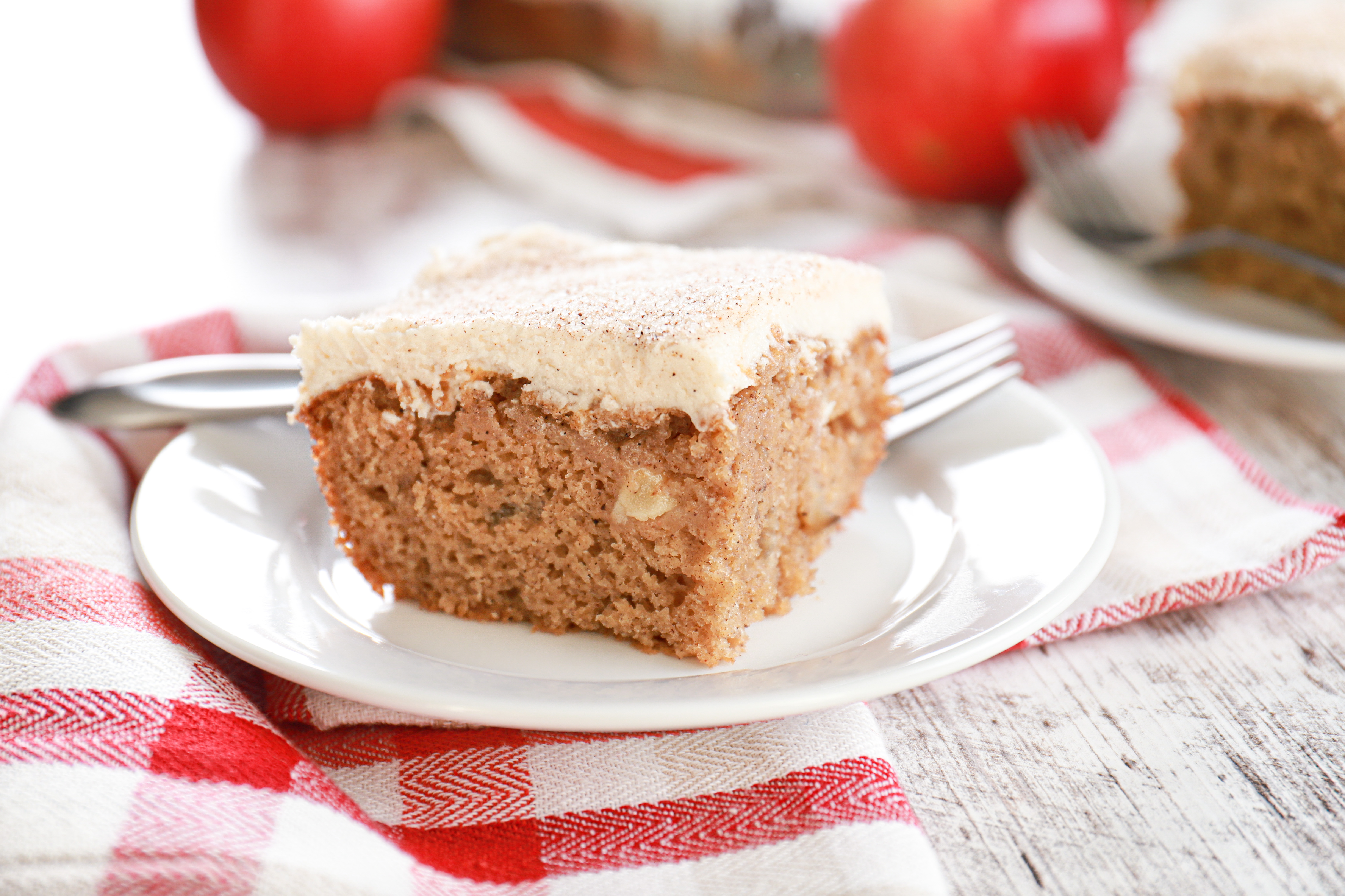 Up close view of a piece of apple cake on a small white plate with baking dish of remaining cake in the background.