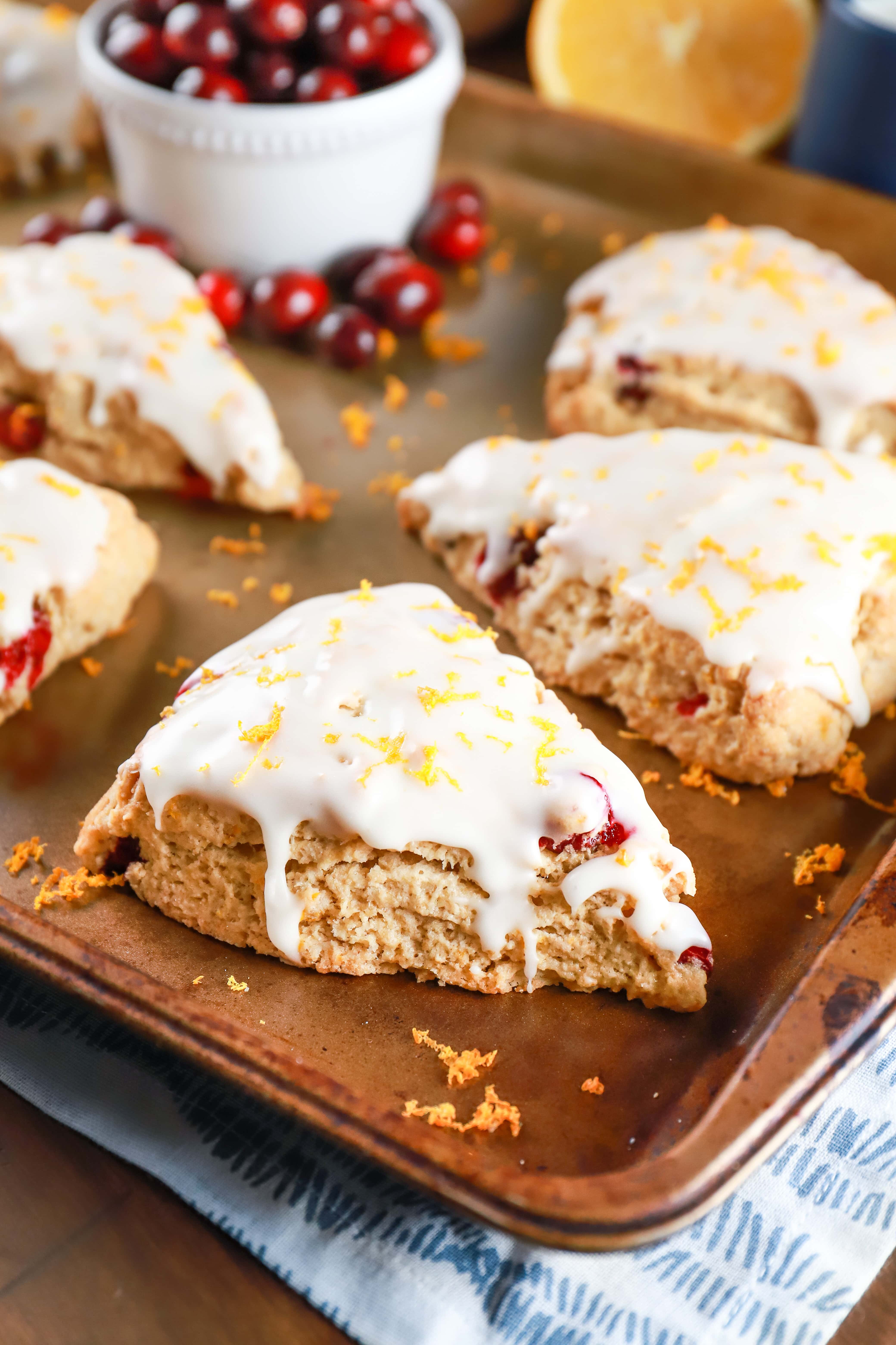 Cranberry Orange Scones on a baking sheet with a cup of cranberries. Recipe from A Kitchen Addiction
