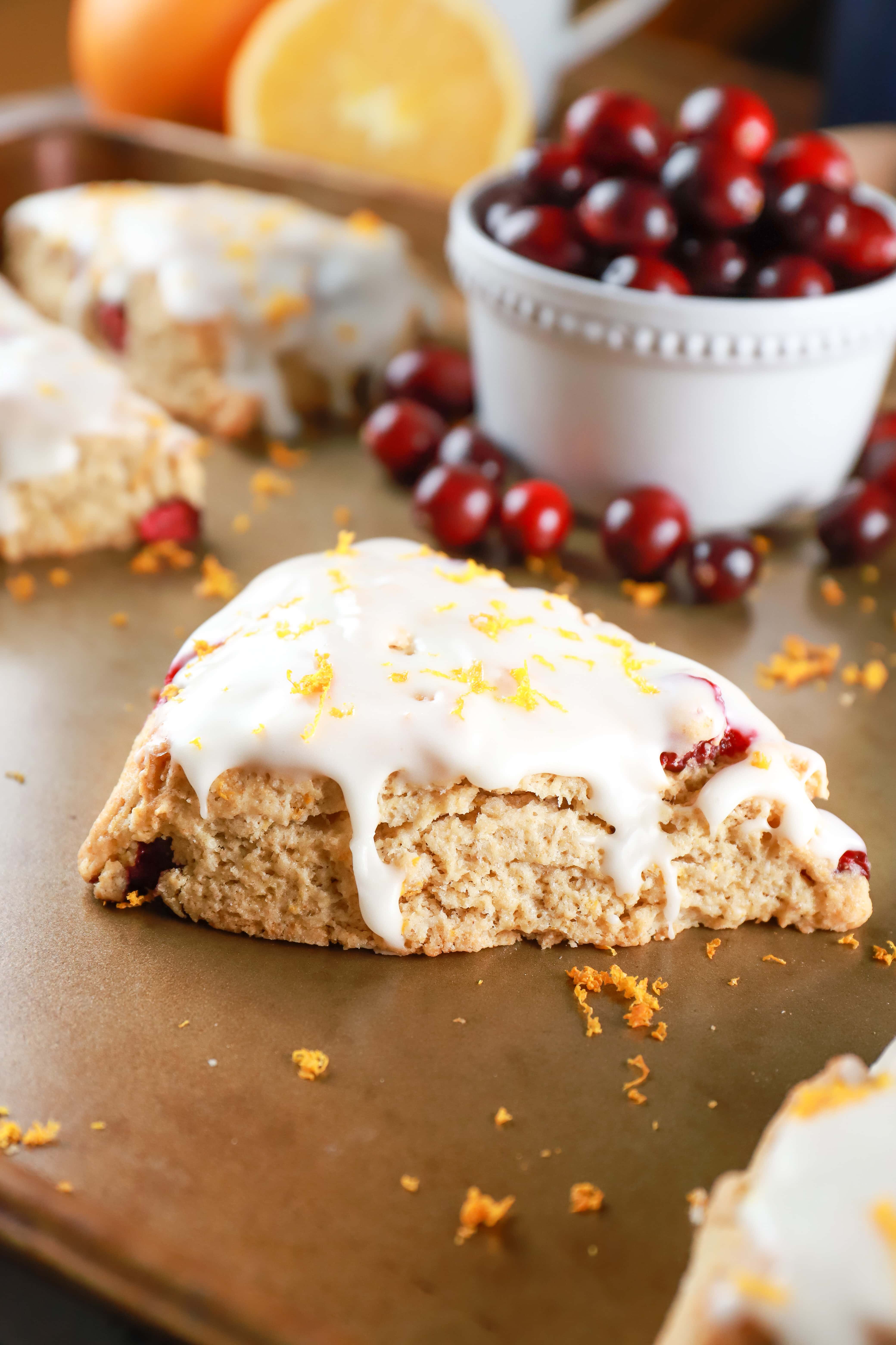 Up close view of a glazed cranberry orange scone on a baking sheet with oranges and cranberries in the background. Recipe from A Kitchen Addiction