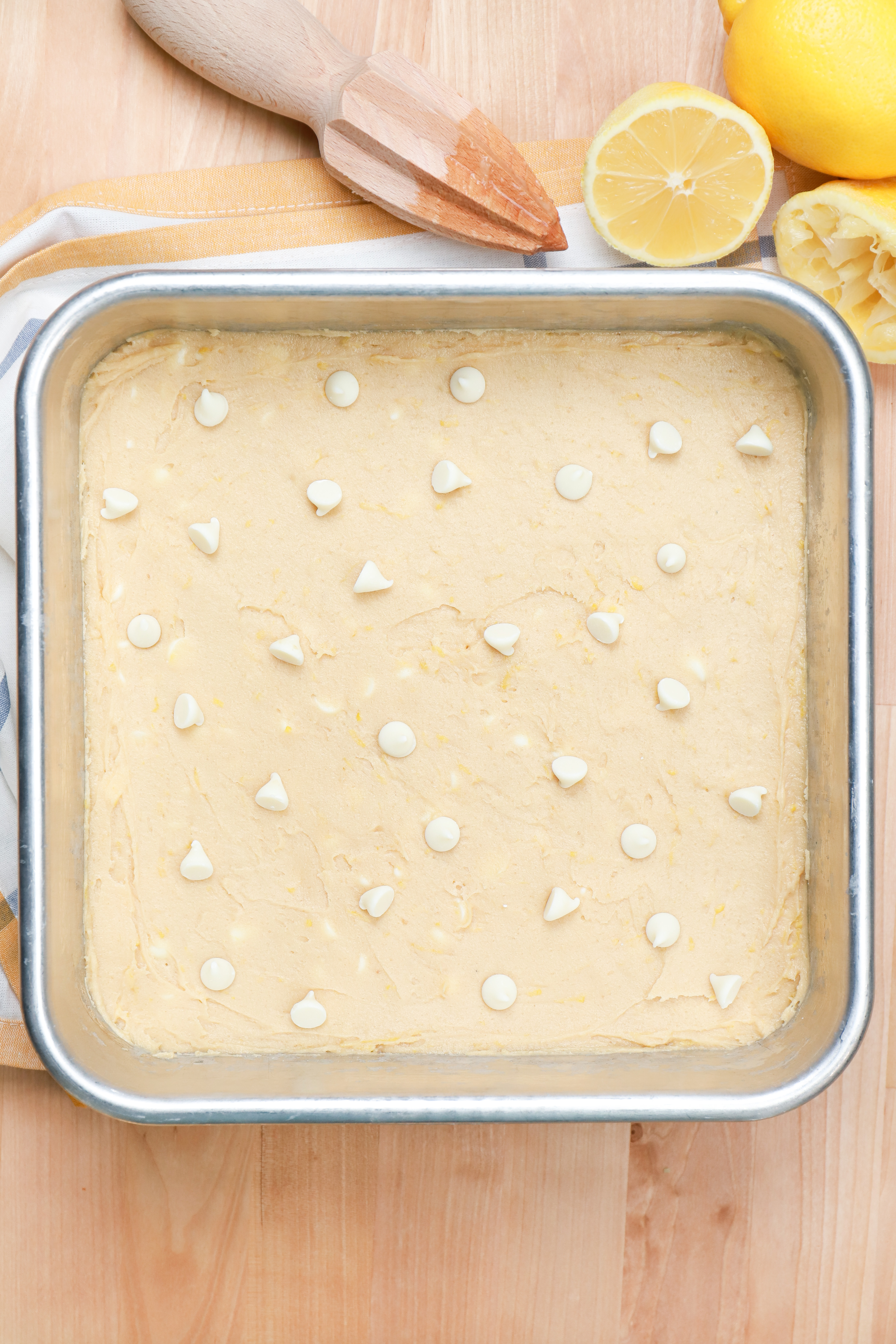 White chocolate lemon blondies dough spread into bottom of aluminum baking dish and sprinkled with white chocolate chips.