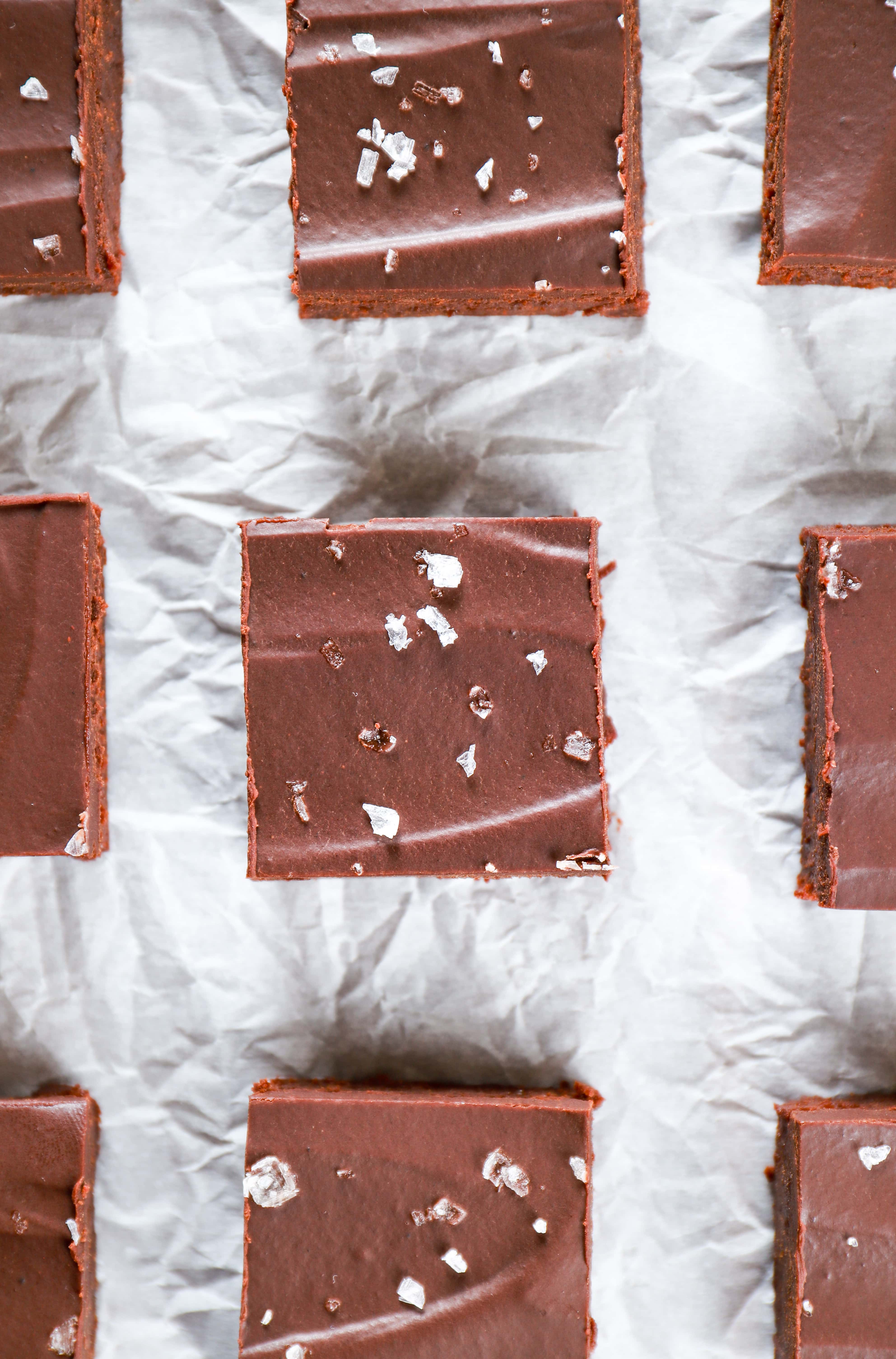 Overhead view of flourless brownies with sea salt ganache on a piece of parchment paper. Recipe for flourless brownies from A Kitchen Addiction