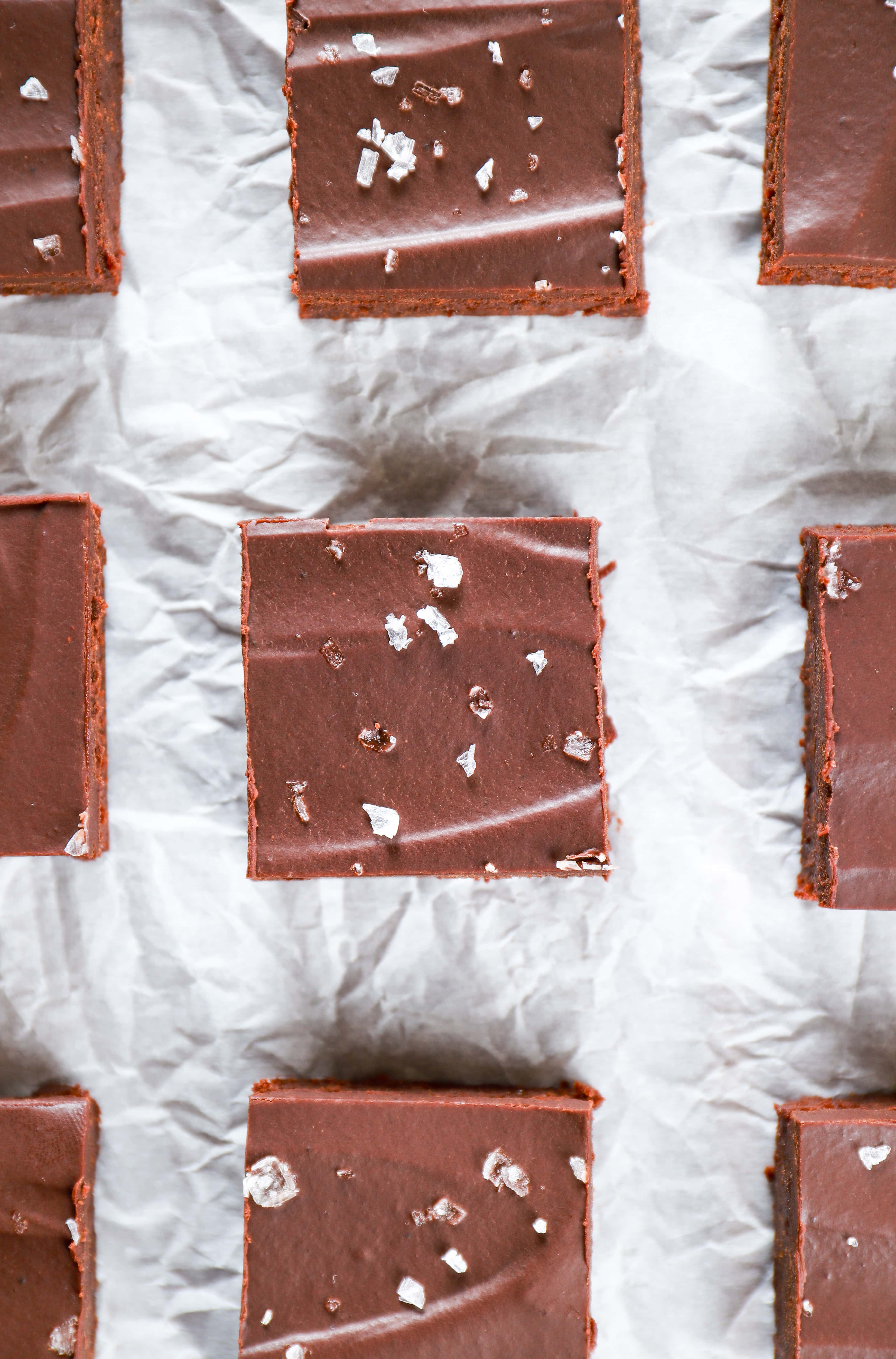 Overhead view of flourless brownies with sea salt ganache on a piece of parchment paper. Recipe for flourless brownies from A Kitchen Addiction