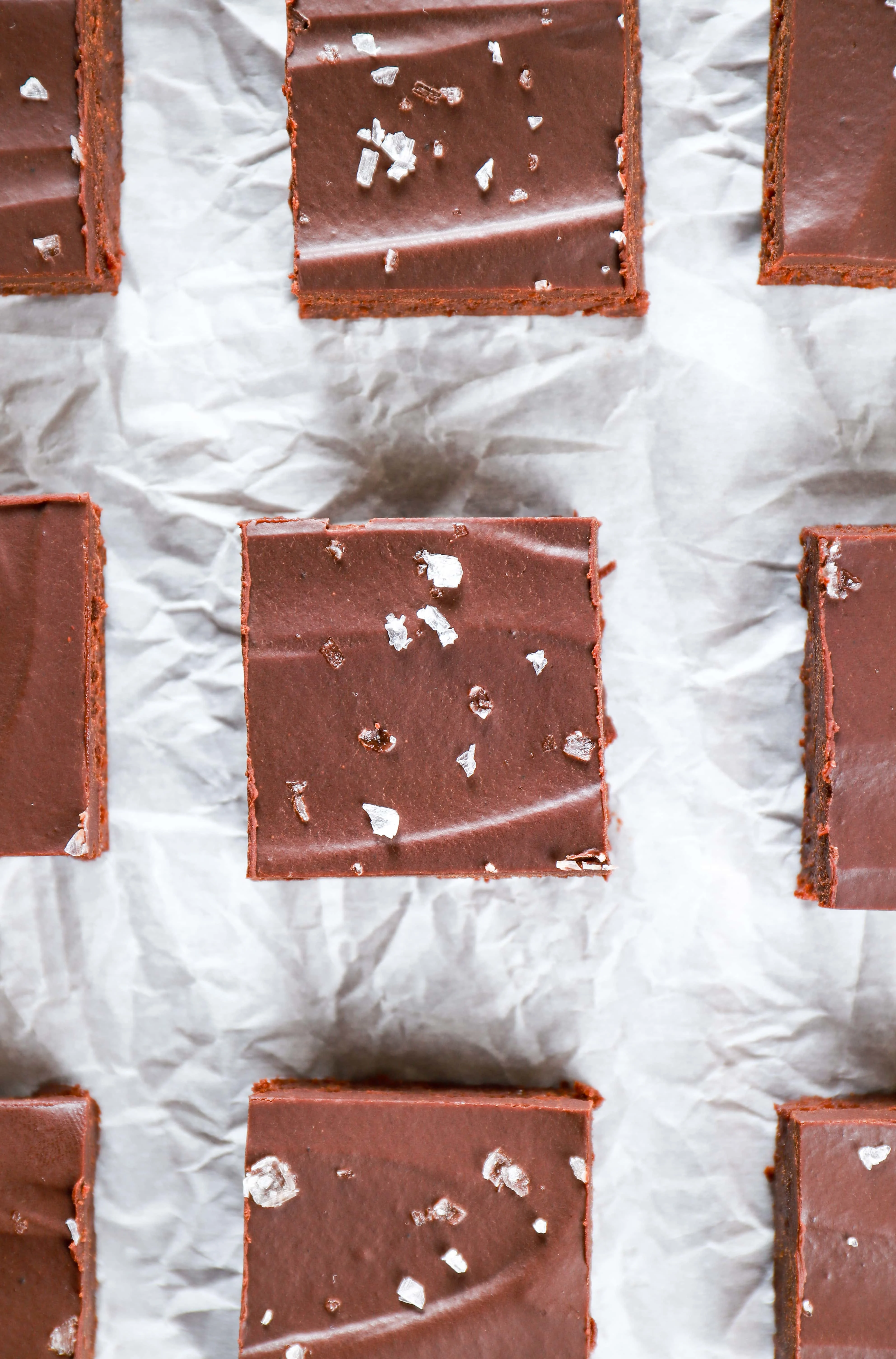 Overhead view of flourless brownies with sea salt ganache on a piece of parchment paper. Recipe for flourless brownies from A Kitchen Addiction