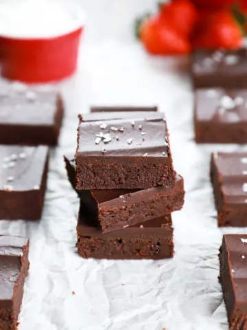 Stack of fudgy flourless brownies on a piece of parchment paper with a colander of strawberries in the background. Recipe from A Kitchen Addiction